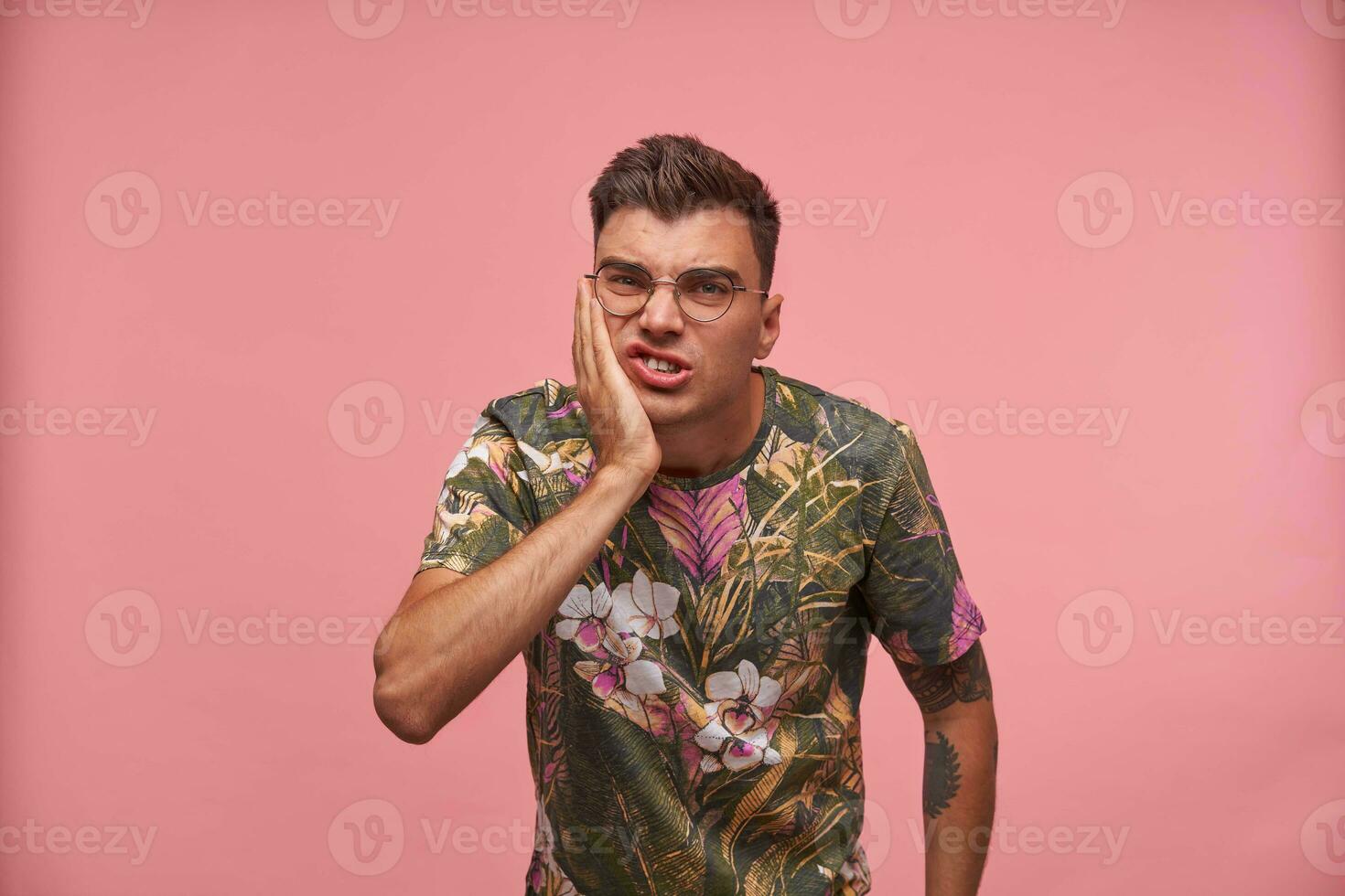 studio tiro di giovane infelice tipo con palma su il suo guancia, sofferenza a partire dal mal di denti, guardare irritato e malato, isolato al di sopra di rosa sfondo foto