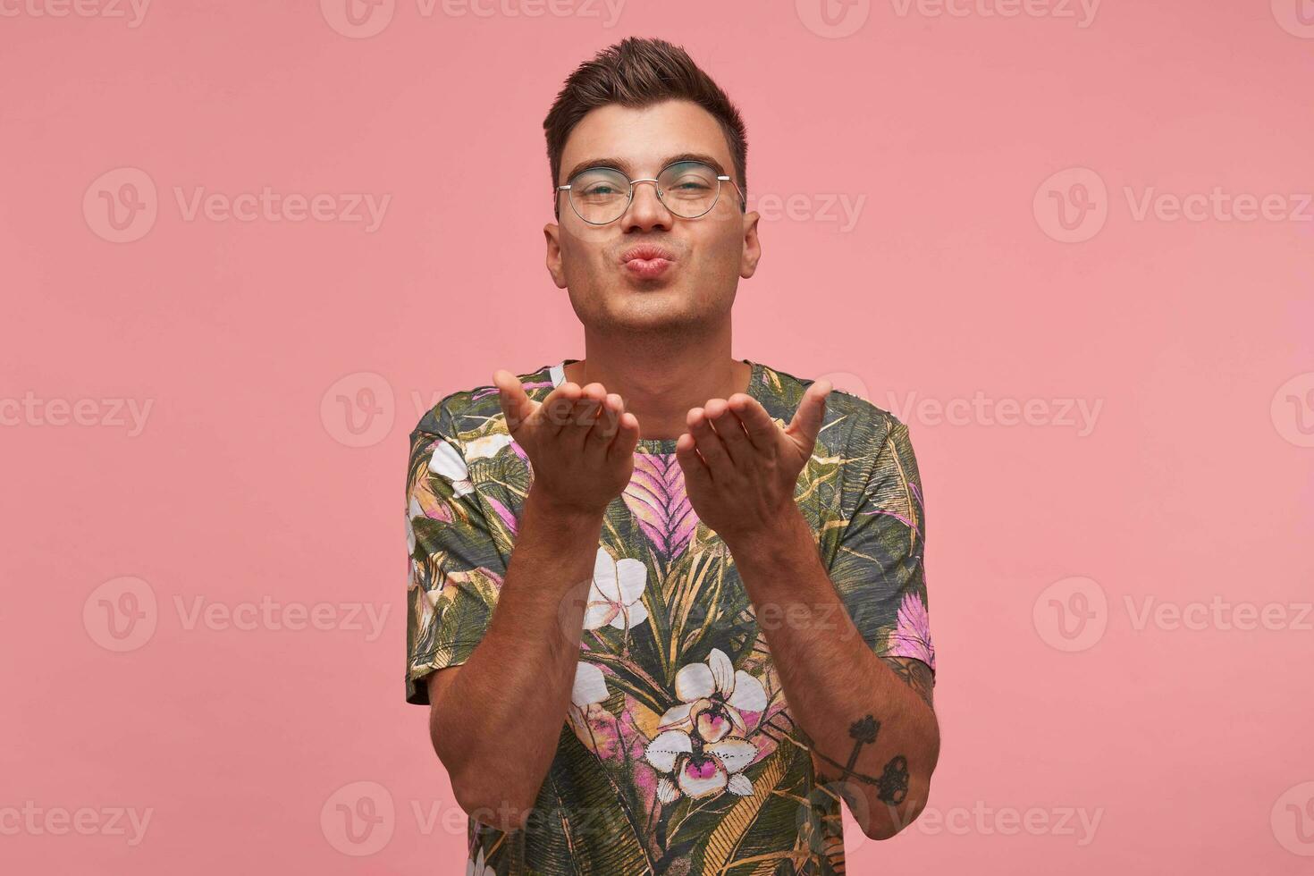 piacevole guardare carino giovane maschio arrotondamento labbra come colpi aria bacio, guardare con amore e simpatia per telecamera, provando per flirtare, isolato al di sopra di rosa studio sfondo foto