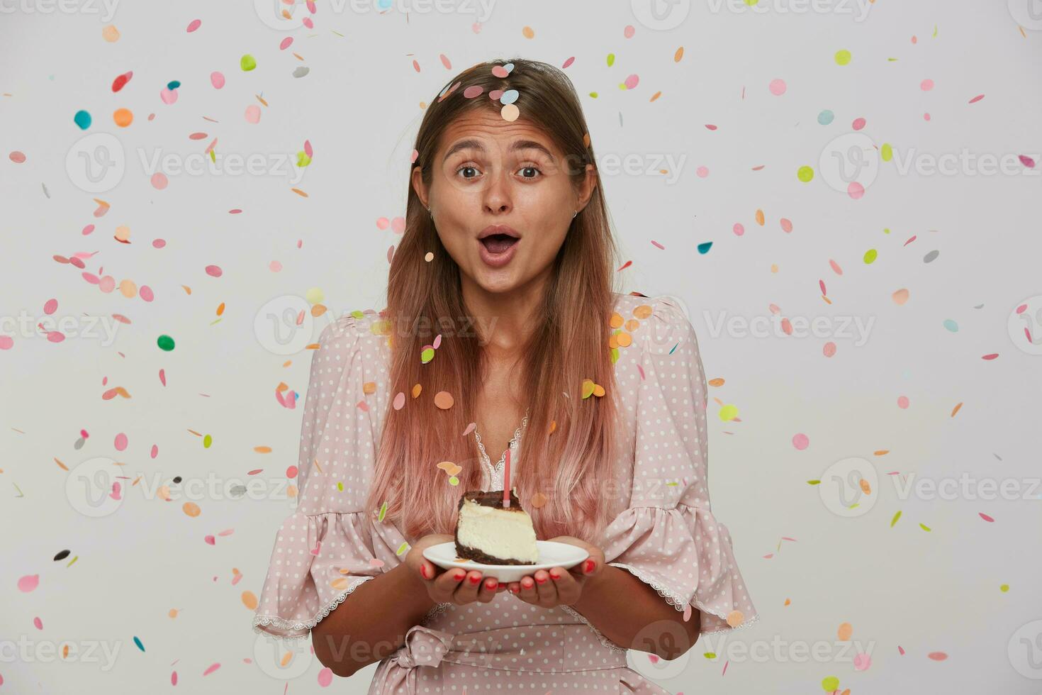 studio tiro di giovane bellissimo lungo dai capelli bionda signora festeggiare sua compleanno con gli amici, in piedi al di sopra di bianca sfondo nel carta coriandoli con torta nel sollevato mani foto