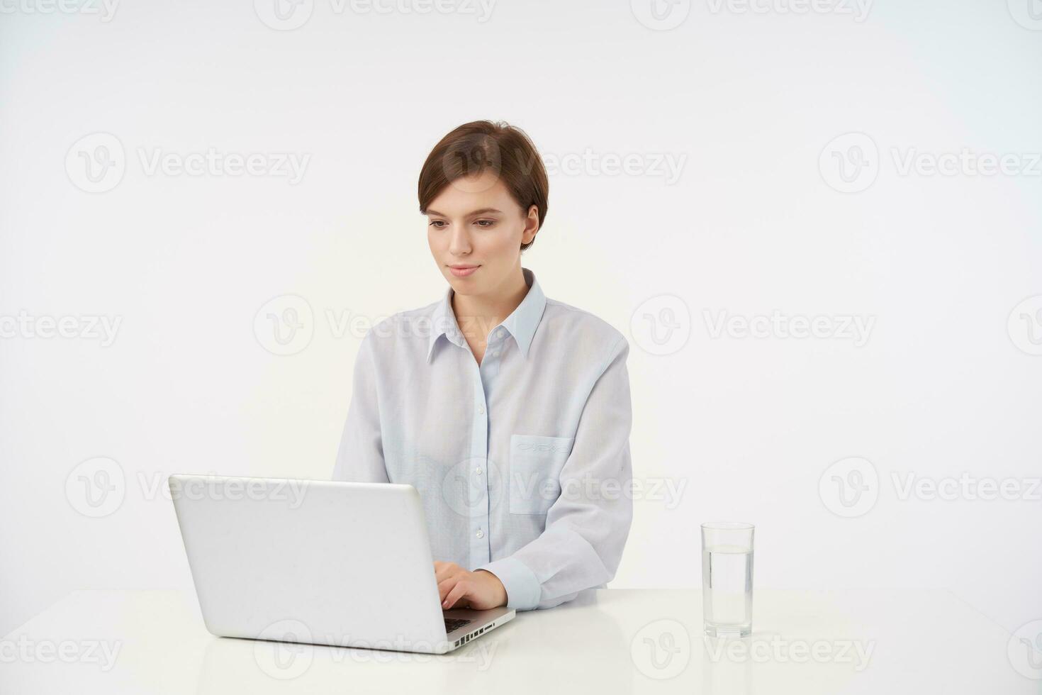 interno foto di affascinante giovane corto dai capelli brunetta signora con casuale acconciatura Tenere sua mano su tastiera e digitando testo su computer portatile, isolato al di sopra di bianca sfondo