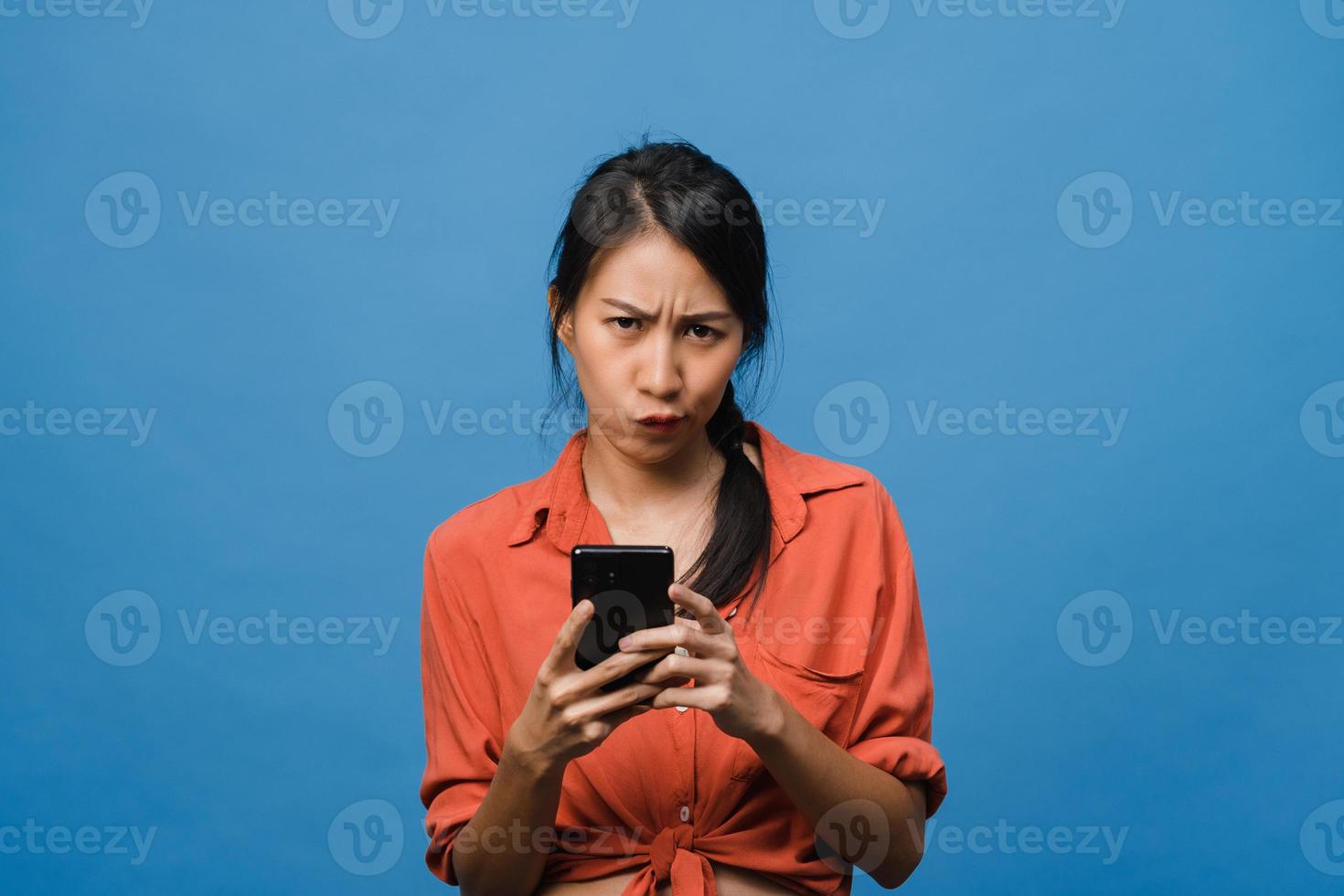 pensando di sognare una giovane donna asiatica che usa il telefono con un'espressione positiva, vestita con abiti casual, sentendo felicità e stando isolata su sfondo blu. felice adorabile donna felice esulta successo. foto