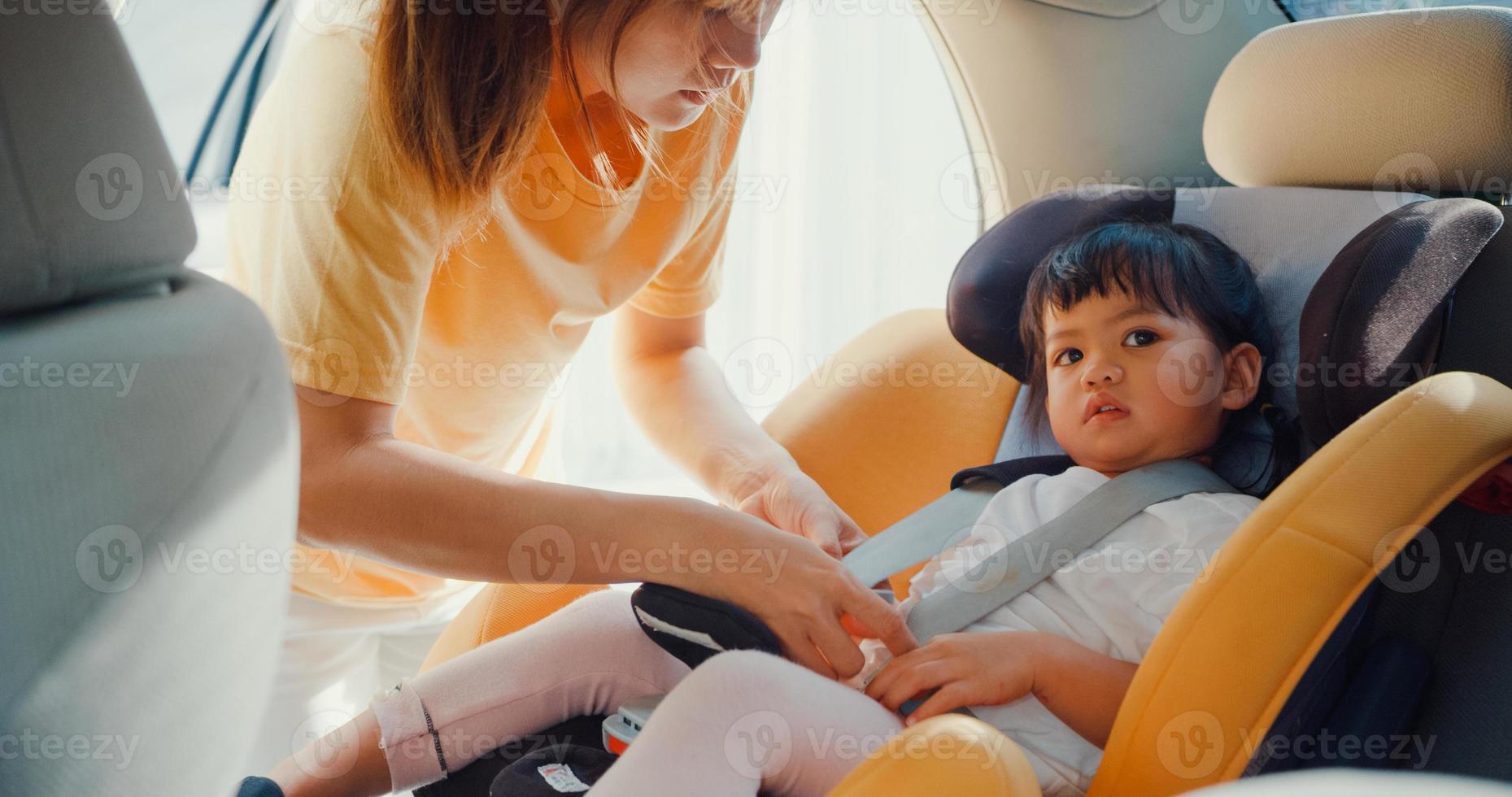 felice allegra famiglia asia mamma che allaccia la cintura di sicurezza del seggiolino auto prima di andare a fare un giro con la bambina che si prepara per il viaggio in auto. concetto di guida sicura. foto