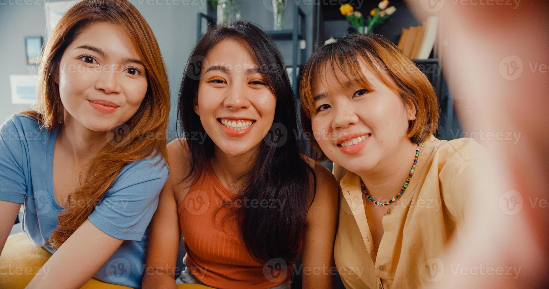 donne asiatiche adolescenti che si sentono selfie sorridenti felici e guardano la telecamera mentre si rilassano nel soggiorno di casa. Videochiamata allegra delle signore del compagno di stanza con l'amico e la famiglia, concetto di stile di vita della donna a casa. foto