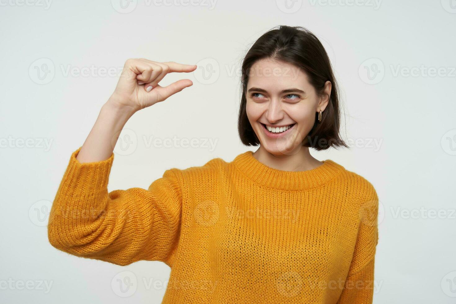 interno tiro di giovane positivo femmina indossa giallo maglione, mostrando piccolo gesto, sorrisi. isolato al di sopra di bianca sfondo foto