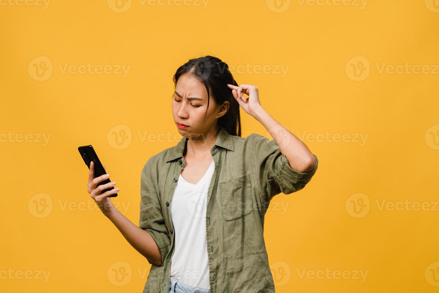 pensando di sognare la giovane donna asiatica che usa il telefono con espressione positiva, vestita con un panno casual sentendo felicità e stando isolata su sfondo giallo. felice adorabile donna felice esulta successo. foto