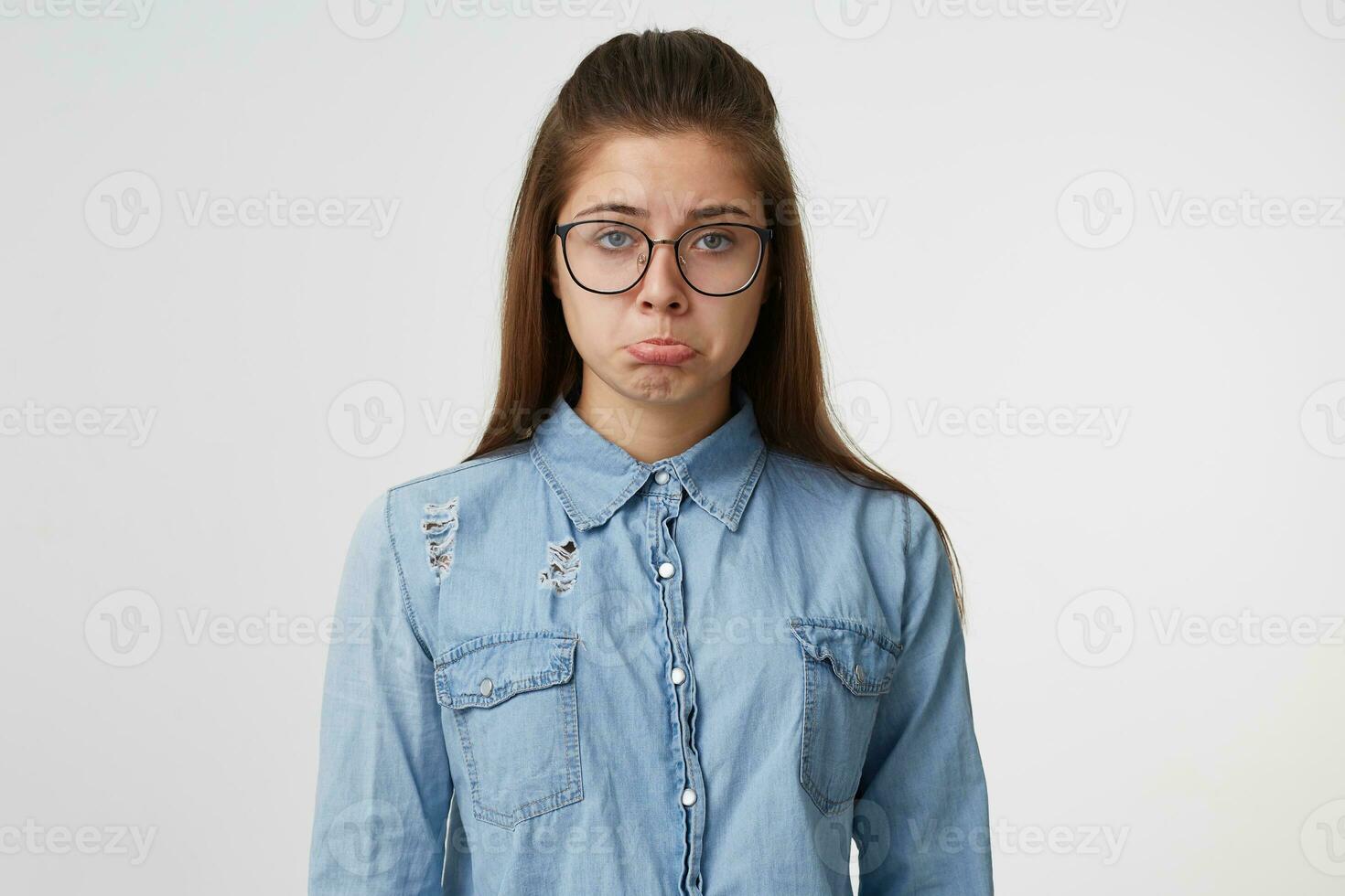 irritato ragazza purtroppo guardare in il telecamera, trasformato su sua inferiore labbro, triste, angosciato, fatto non ottenere sua premio, vestito nel un' denim camicia, isolato su un' bianca sfondo foto