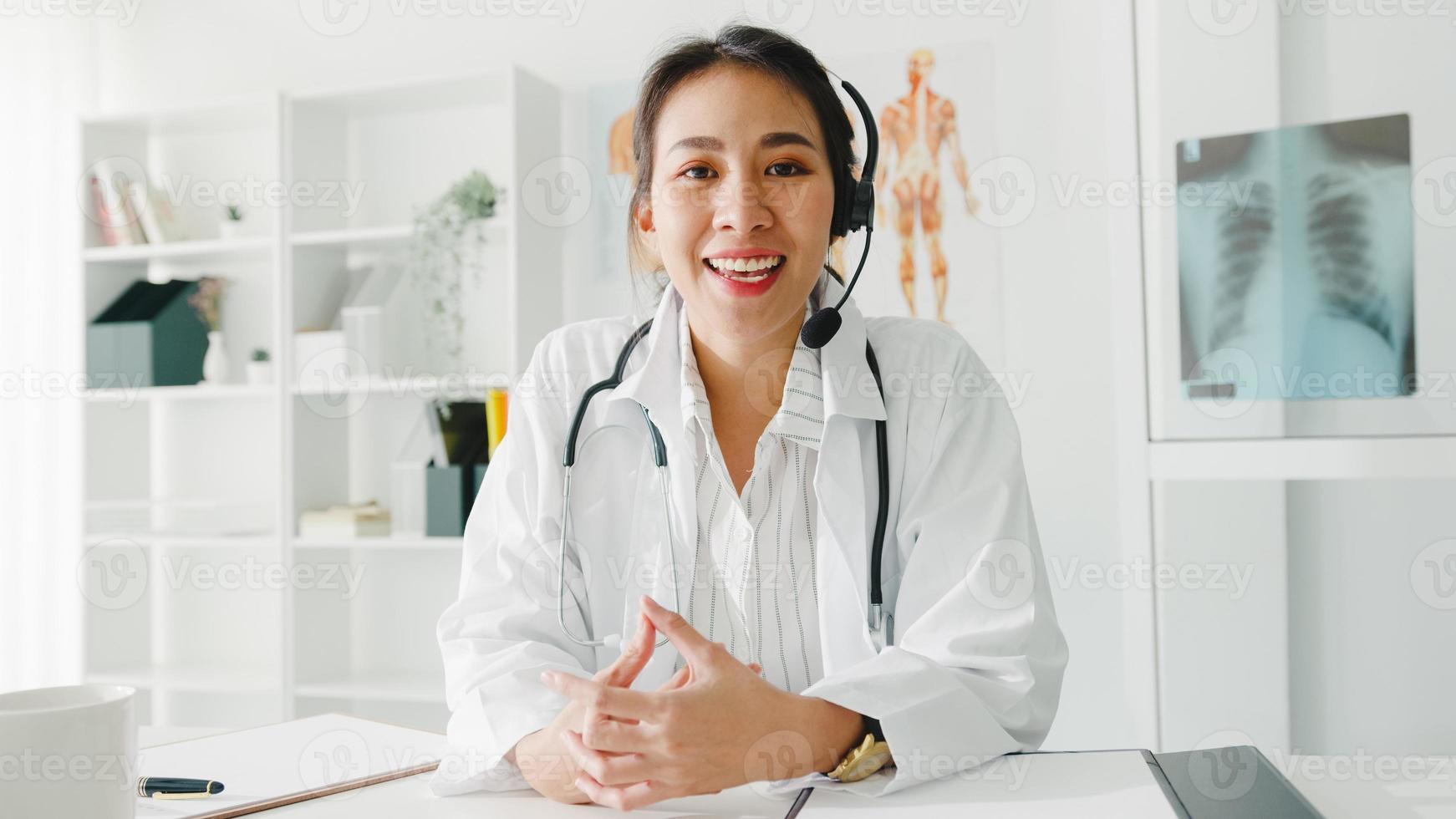 giovane dottoressa asiatica in uniforme medica bianca con stetoscopio utilizzando il computer portatile parla in videoconferenza con il paziente, guardando la telecamera in ospedale sanitario. concetto di consulenza e terapia. foto