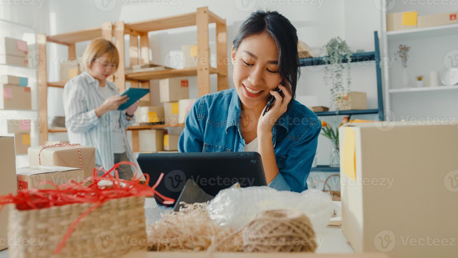 giovani imprenditrici asiatiche che utilizzano la chiamata di telefonia mobile che ricevono l'ordine di acquisto e controllano il prodotto in magazzino lavorano a casa. piccolo imprenditore, consegna al mercato online, concetto di lifestyle freelance. foto