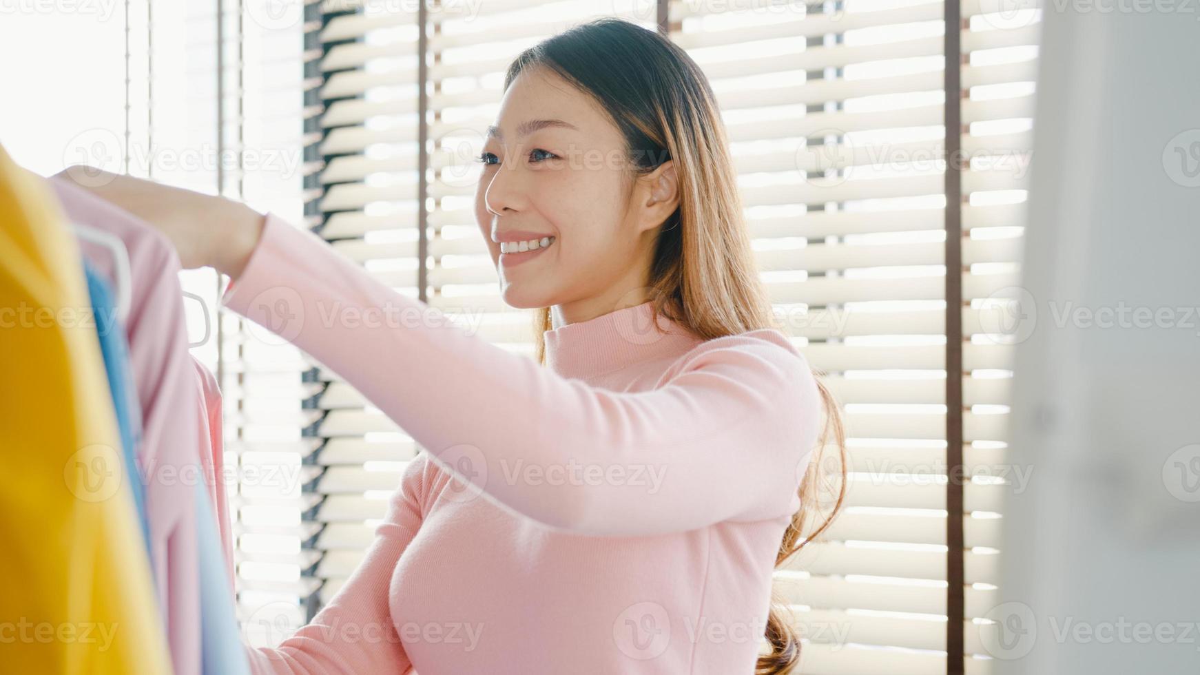 bella giovane signora asiatica attraente che sceglie i suoi vestiti di vestito di moda nell'armadio a casa o in negozio. ragazza pensa a cosa indossare camicia casual. guardaroba di casa o spogliatoio del negozio di abbigliamento. foto