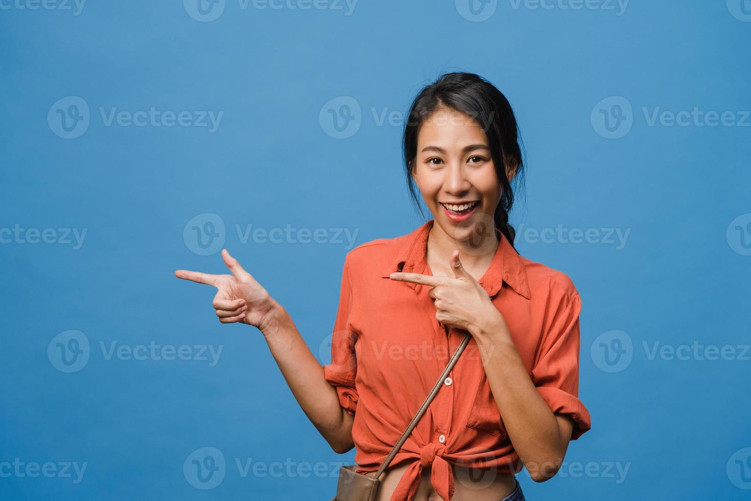 ritratto di giovane donna asiatica sorridente con espressione allegra, mostra qualcosa di straordinario nello spazio vuoto in un panno casual e guardando la telecamera isolata su sfondo blu. concetto di espressione facciale. foto