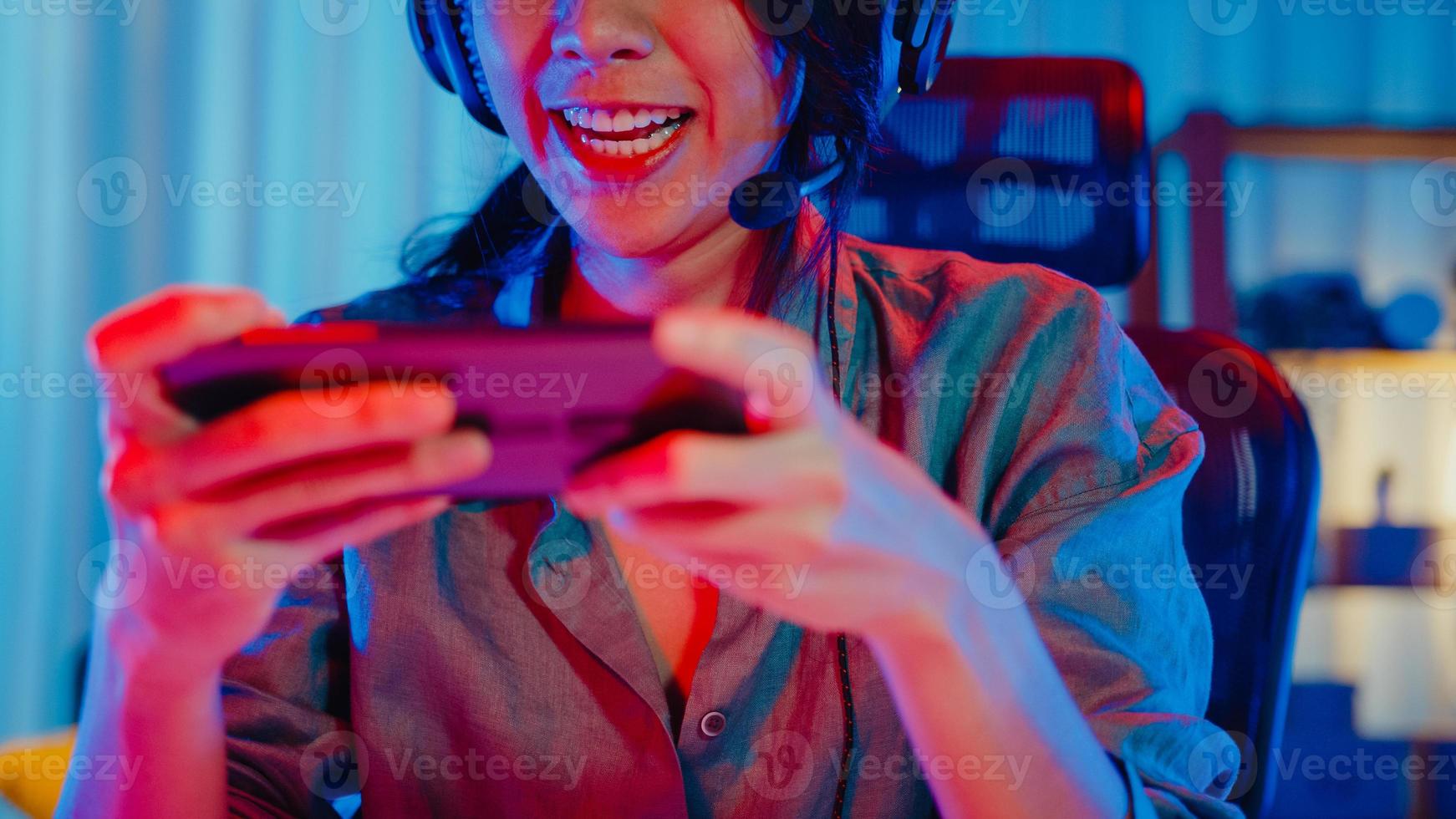 felice asia ragazza giocatore indossa la competizione per le cuffie gioca al videogioco online con smartphone luci al neon colorate nel soggiorno di casa. gioco in streaming di esport online, concetto di attività di quarantena domestica. foto