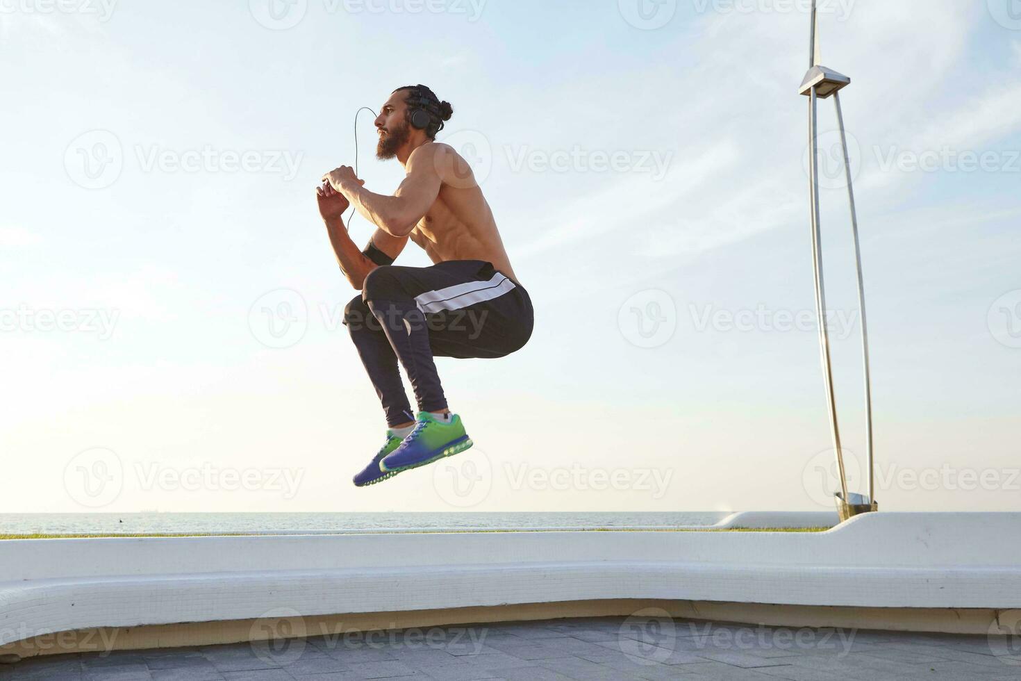 foto di giovane barbuto salto tipo con in forma atletico corpo, facendo mattina esercizi, ha muscolare corpo forma, ascoltando musica su cuffia.