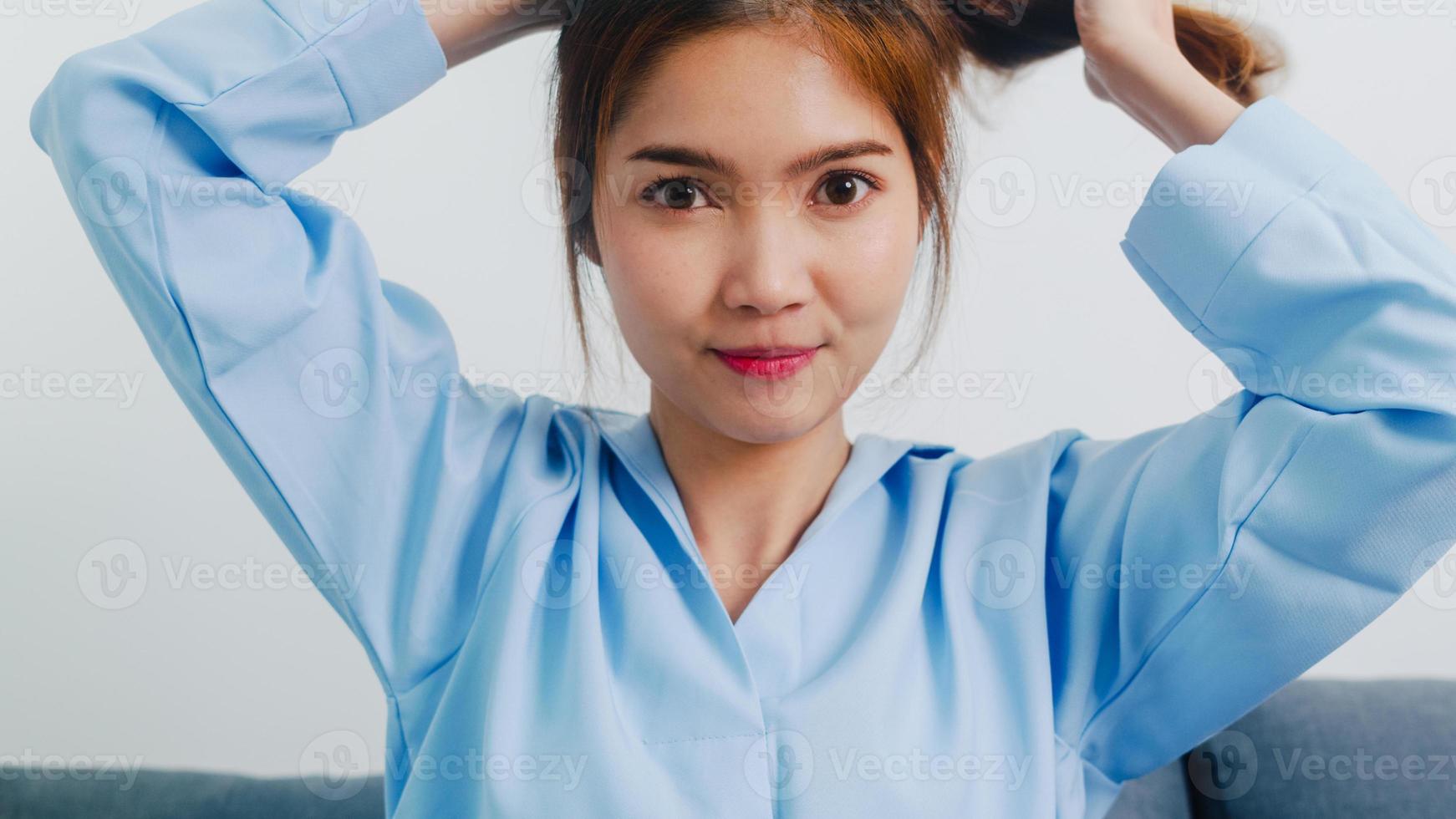 giovane donna asiatica che fa stile di capelli lunghi guardando davanti allo specchio, la femmina felice fa l'acconciatura a coda di cavallo per migliorare se stessa pronta a lavorare in camera da letto a casa. donne di stile di vita a casa concetto. foto