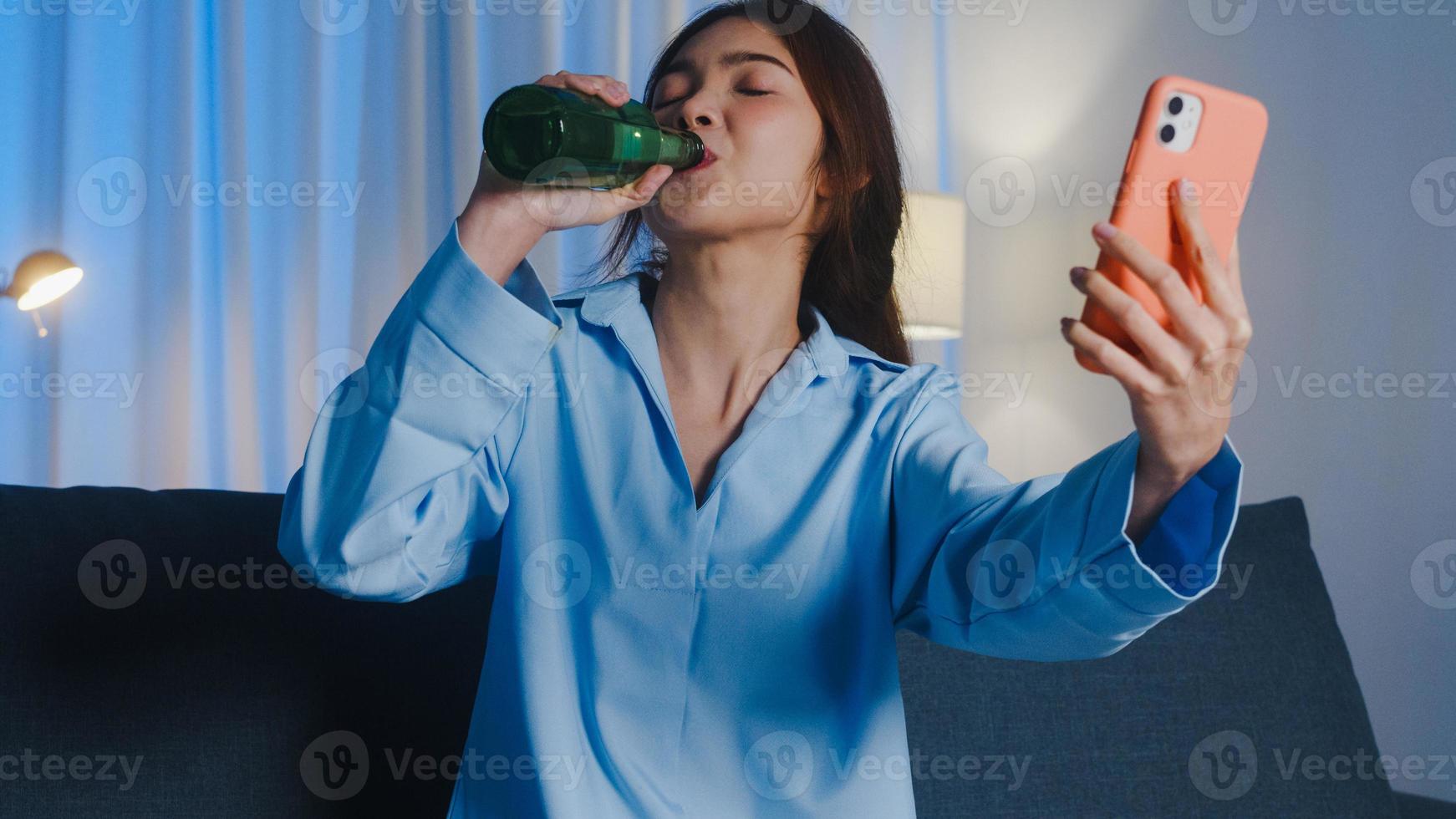 giovane donna asiatica che beve birra divertirsi momento felice festa notturna evento celebrazione online tramite videochiamata nel soggiorno di casa di notte. distanziamento sociale, quarantena per la prevenzione del coronavirus. foto