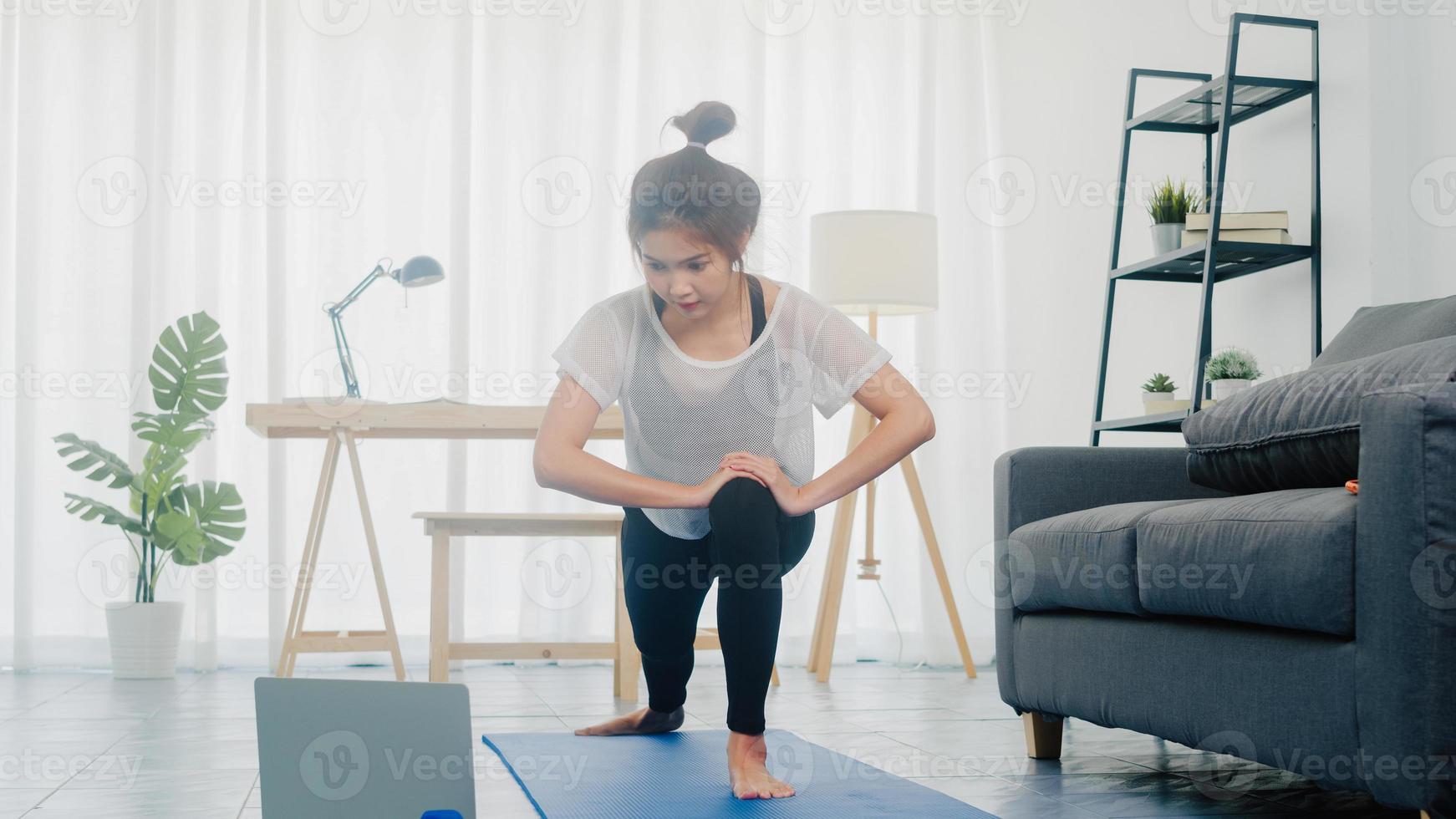 giovane donna coreana in esercizi di abbigliamento sportivo facendo allenamento e usando il laptop per guardare video tutorial di yoga a casa. formazione a distanza con personal trainer, distanza sociale, concetto di educazione online. foto