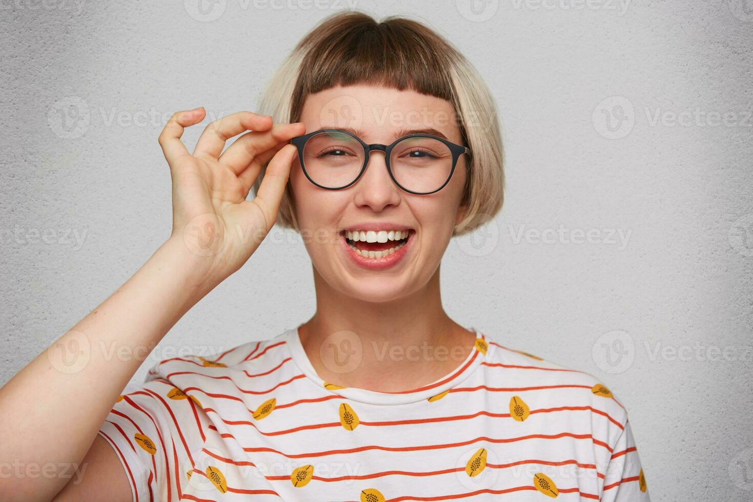avvicinamento di contento bella giovane donna indossa a strisce t camicia e spettacoli si sente rilassato, ridendo e sembra direttamente nel telecamera isolato al di sopra di bianca sfondo foto