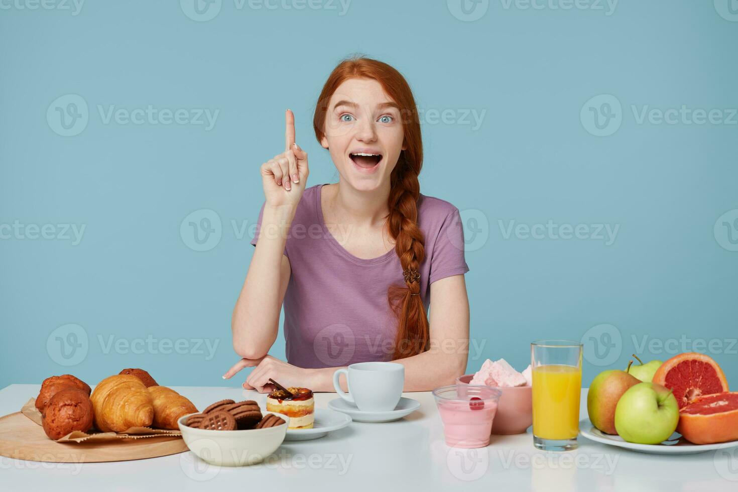 giovane carino ispirato eccitato dai capelli rossi ragazza seduta a il tavolo durante prima colazione. un' bene idea si è verificato per suo, sollevato sua indice dito verso l'alto, su il tavolo posare pasticcini e fresco salutare prodotti. foto