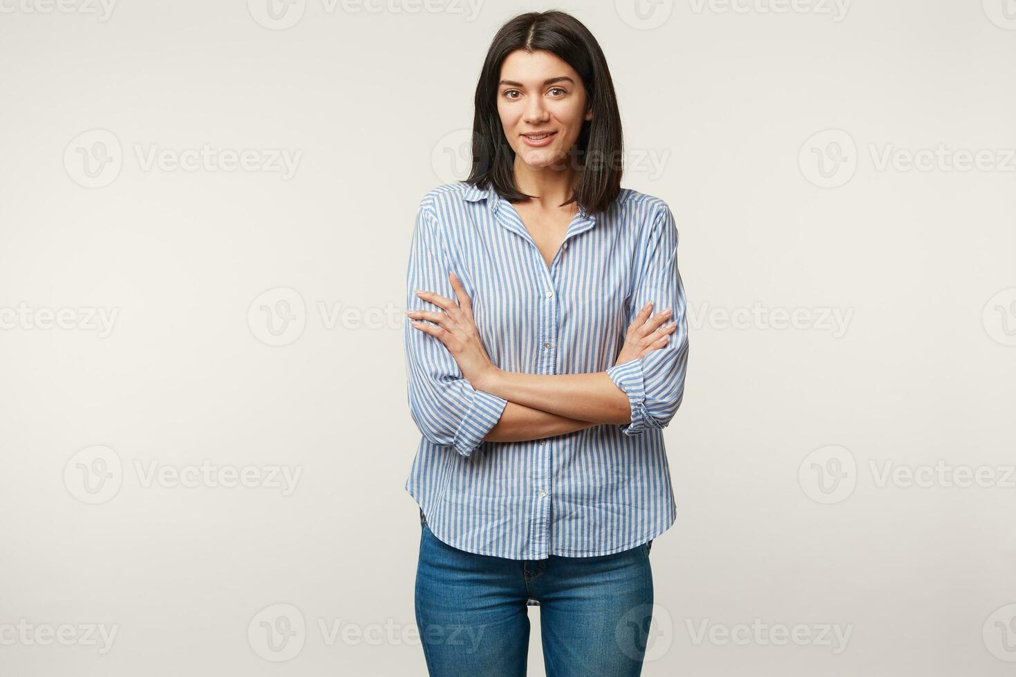 genere piacevole giovane dai capelli scuri femmina in piedi con braccia attraversato vestito nel jeans e a strisce camicia bocca ha aperto come parlando con qualcuno, sensazione un' poco malato a sollievo, isolato al di sopra di bianca parete foto