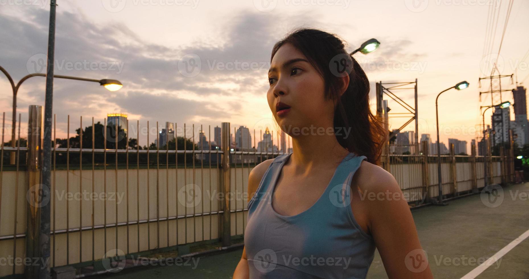 bella giovane donna atleta asiatica si esercita perché si sente stanca dopo aver corso in ambiente urbano. la ragazza teenager giapponese si allena indossando abiti sportivi sul ponte pedonale al mattino presto. foto