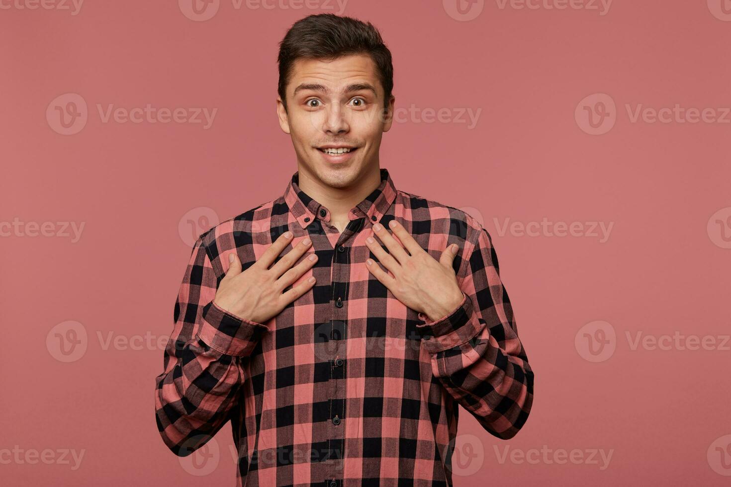 giovane bello stupito tipo indossa nel scacchi camicia, sembra a il telecamera con contento espressione, punto a lui stesso, isolato al di sopra di rosa sfondo. foto