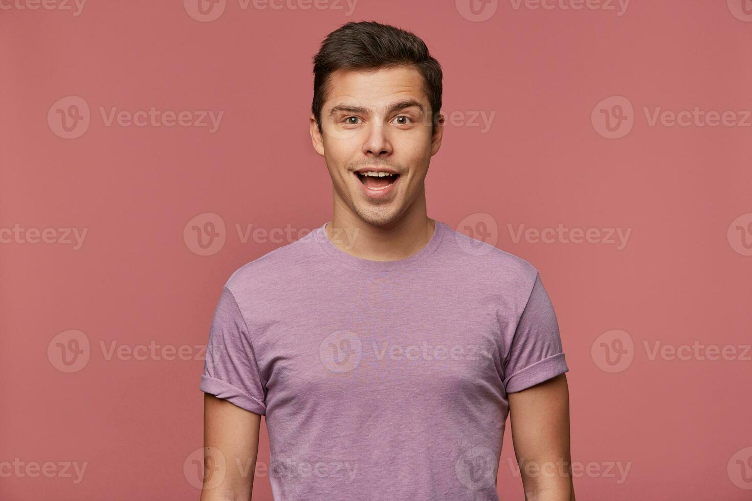 ritratto di bello allegro tipo indossa nel vuoto maglietta, sembra a il telecamera con contento stupito espressione, sta al di sopra di rosa sfondo. foto