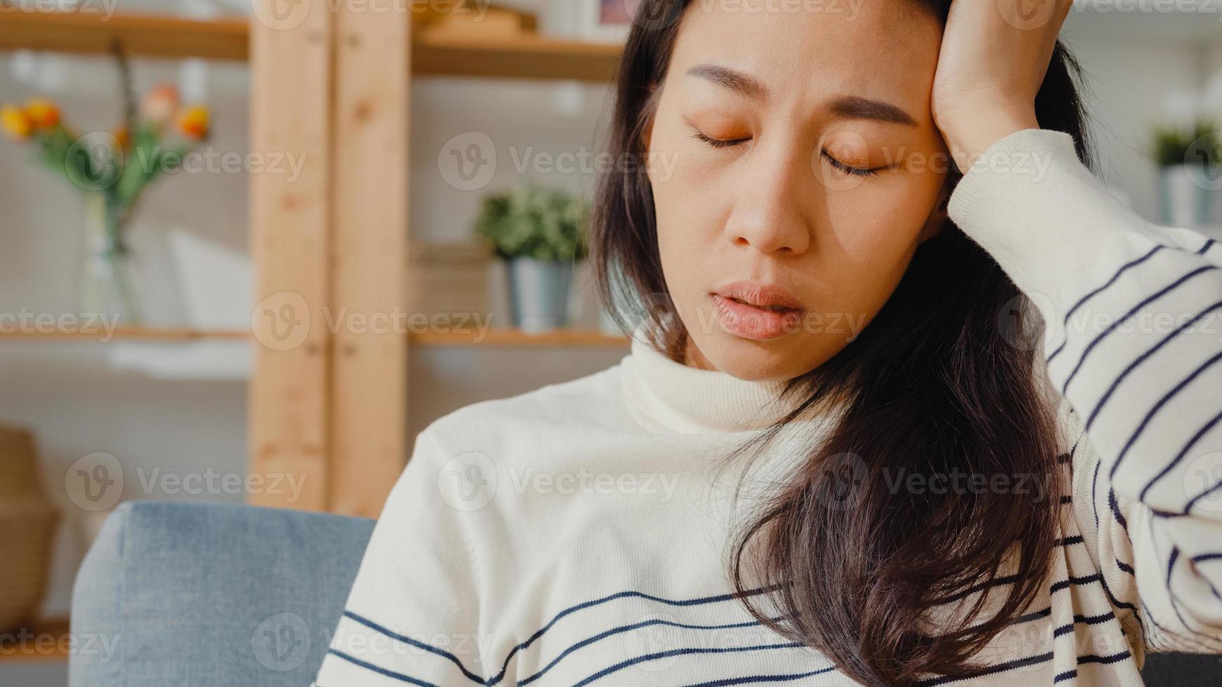 premurosa signora asiatica si siede abbracciando le ginocchia al divano nel soggiorno a casa guarda fuori con sentirsi solo, triste adolescente depresso trascorrere del tempo da solo stare a casa, distanza sociale, quarantena del coronavirus. foto