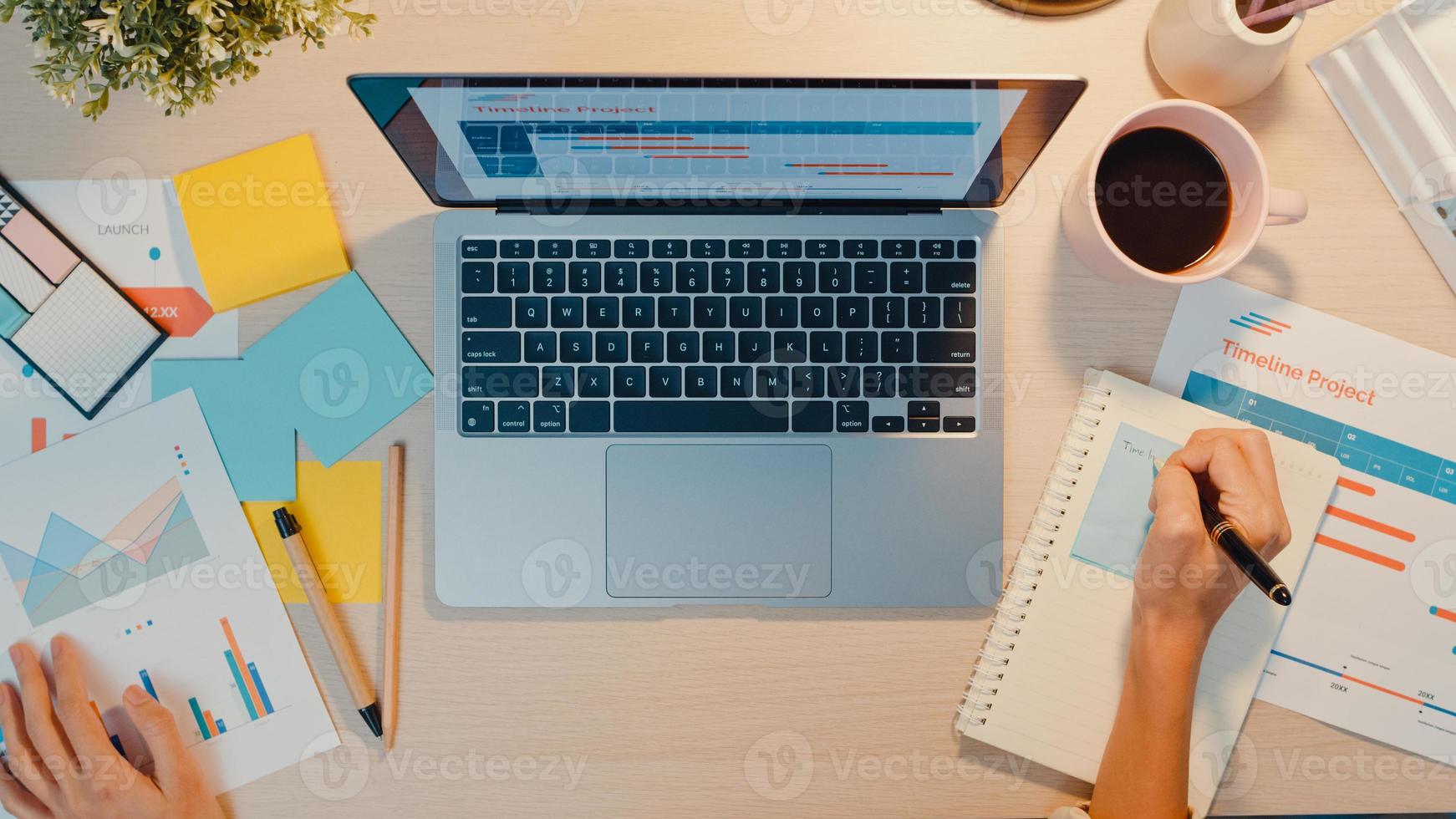 vista dall'alto della giovane donna d'affari asia freelance focus sul laptop scrivere foglio di lavoro grafico finanziario grafico del conto piano di mercato in ufficio notte. lavorare da casa, da remoto, concetto di coronavirus per l'istruzione a distanza foto