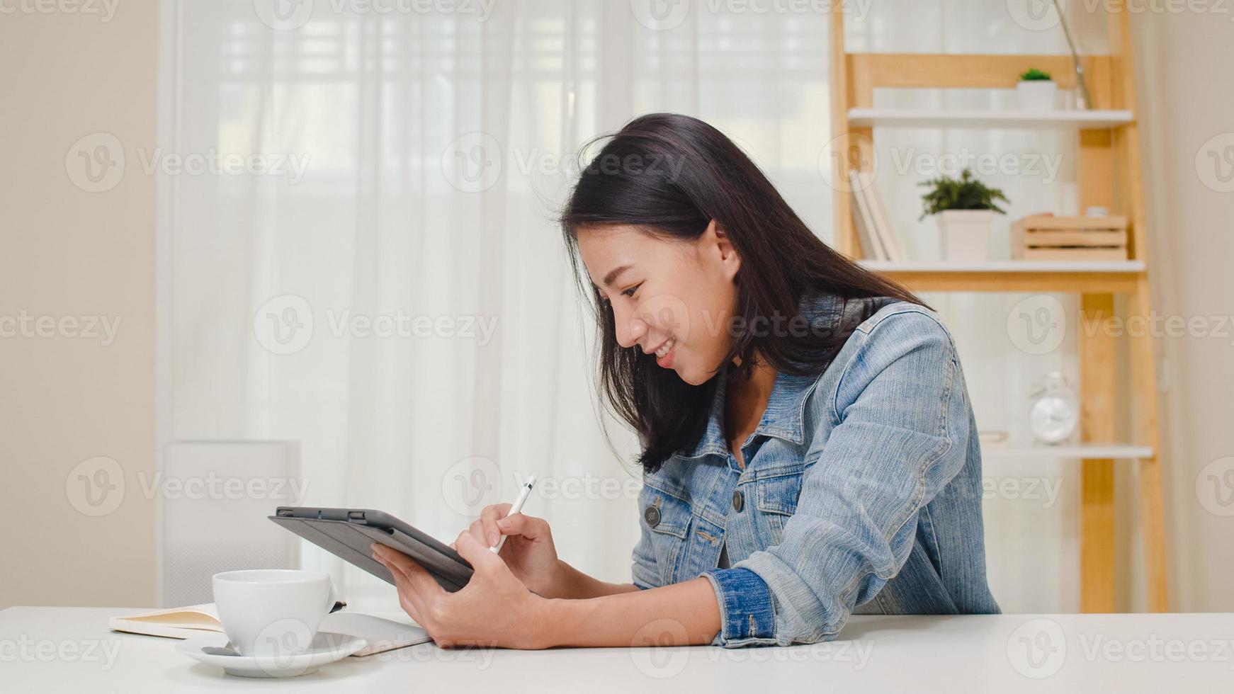 freelance graphic designer donne abbigliamento casual utilizzando tavoletta grafica digitale disegno sul posto di lavoro nel soggiorno di casa. felice giovane ragazza asiatica rilassarsi seduto sulla scrivania fare un lavoro in internet. foto