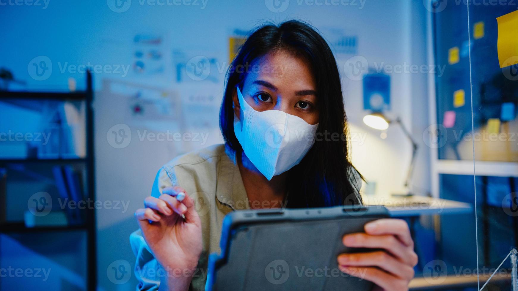 asia imprenditrice indossare maschera facciale distanza sociale in situazione per la prevenzione dei virus guardando la presentazione della fotocamera agli amici sul piano in videochiamata mentre si lavora in ufficio. la vita dopo il corona virus. foto