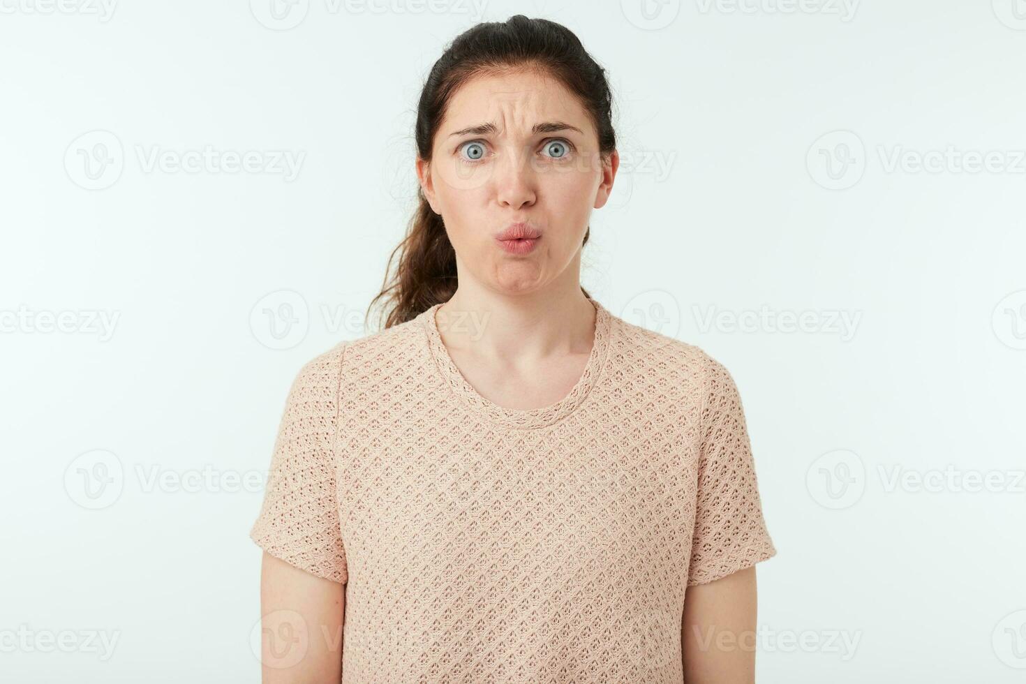 scoraggiato giovane bella Marrone dai capelli femmina accigliato sua sopracciglia mentre guardare confusamente a telecamera, vestito nel beige maglietta mentre in posa al di sopra di bianca sfondo foto