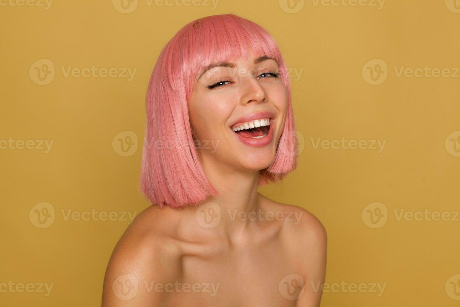 bene guardare giovane contento bella signora con corto rosa capelli lancio indietro sua testa mentre ridendo allegramente, essere nel simpatico umore mentre in posa al di sopra di mostarda sfondo foto