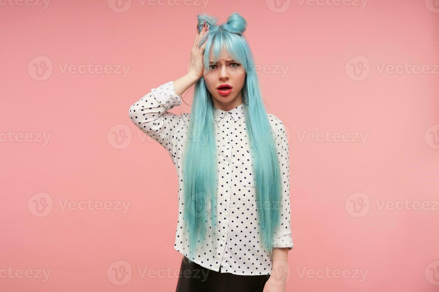 confuso giovane attraente donna con blu anime capelli Tenere palma su sua testa e guardare perplesso per telecamera, accigliato sopracciglia mentre in piedi al di sopra di rosa sfondo foto