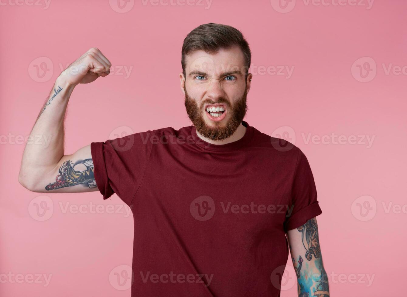 giovane il male rosso barbuto uomo nel vuoto maglietta, sta al di sopra di rosa sfondo, sembra freddo, godere lui stesso e dimostrare potente, sembra a il telecamera e urlando. foto