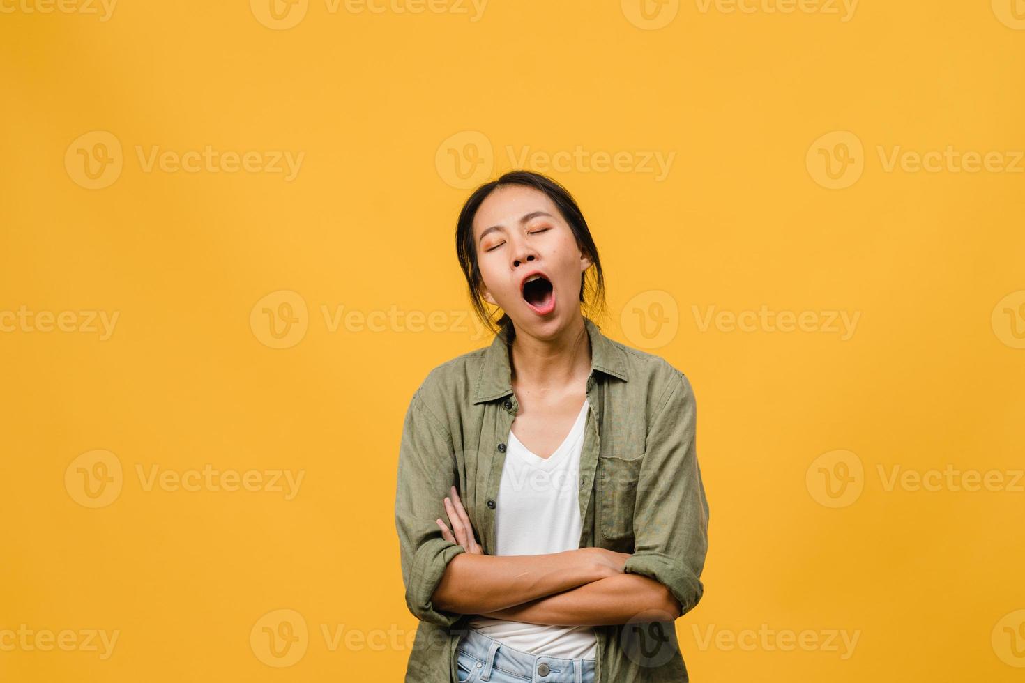 ritratto di giovane donna asiatica con espressione negativa, annoiato sbadigliando stanco che copre la bocca con la mano in abbigliamento casual isolato su sfondo giallo con spazio vuoto per copia. concetto di espressione facciale foto
