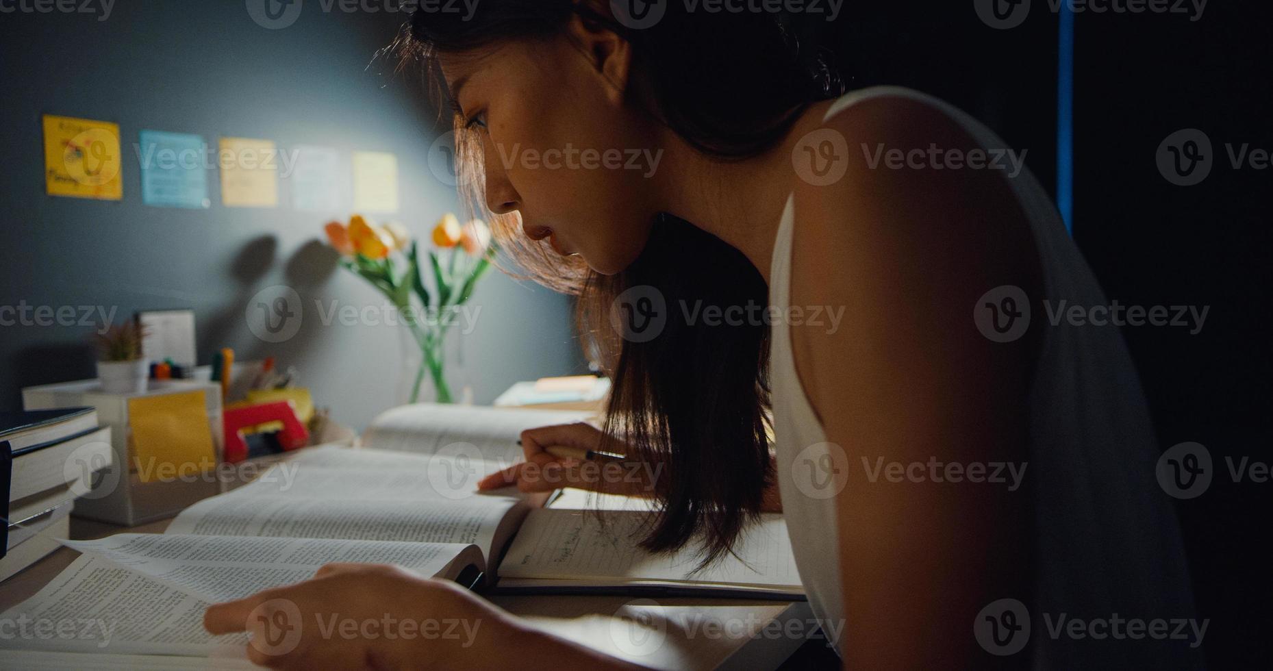 giovane asia teen girl studente lezione di apprendimento a distanza e fare i compiti seduto alla scrivania in soggiorno a casa la notte. lavoro da casa, distanza sociale, quarantena per la prevenzione del virus corona. foto