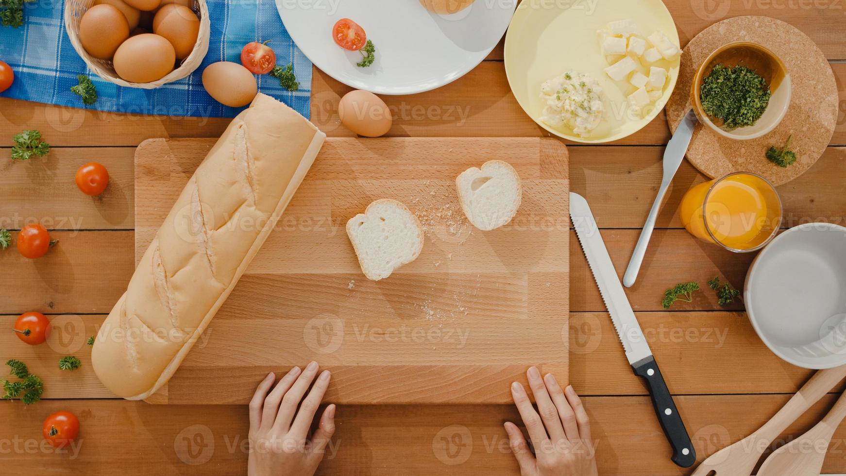 giovane donna asiatica chef spalmare il burro su pane di segale rustico con coltello di metallo su tavola di legno sul tavolo della cucina in casa. produzione di pane fresco fatto in casa, alimentazione sana e panificazione tradizionale. colpo di vista dall'alto. foto