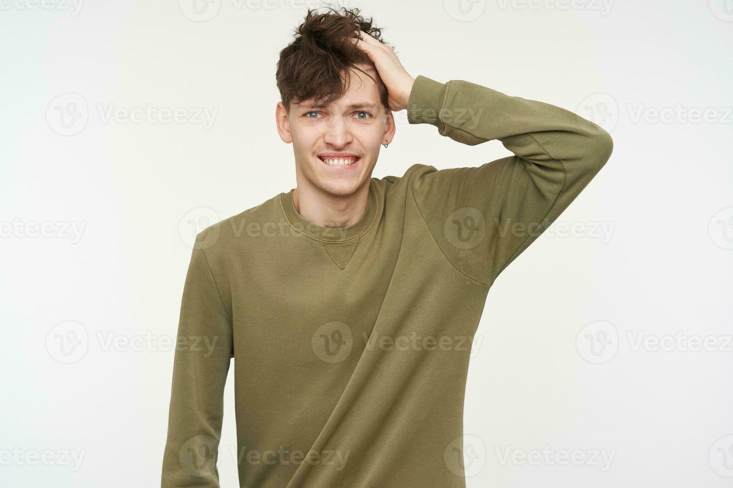 confuso guardare maschio, bello tipo con brunetta capelli, penetrante e setola. indossare cachi colore maglione. toccante lui è aveva e pungente un' labbro. Guardando a il telecamera isolato al di sopra di bianca sfondo foto