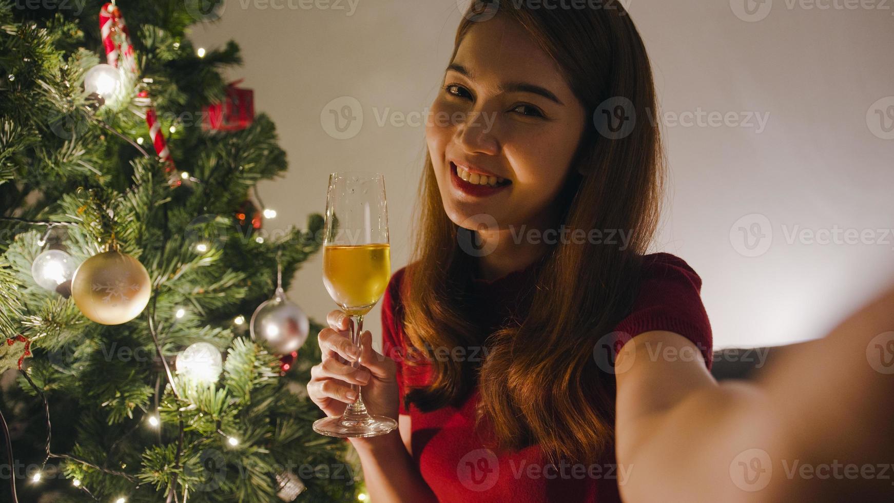 giovane donna asiatica che beve vino divertendosi felice notte festa videochiamata parlare con coppia, albero di Natale decorato con ornamenti nel soggiorno di casa. festa di Natale e Capodanno. foto