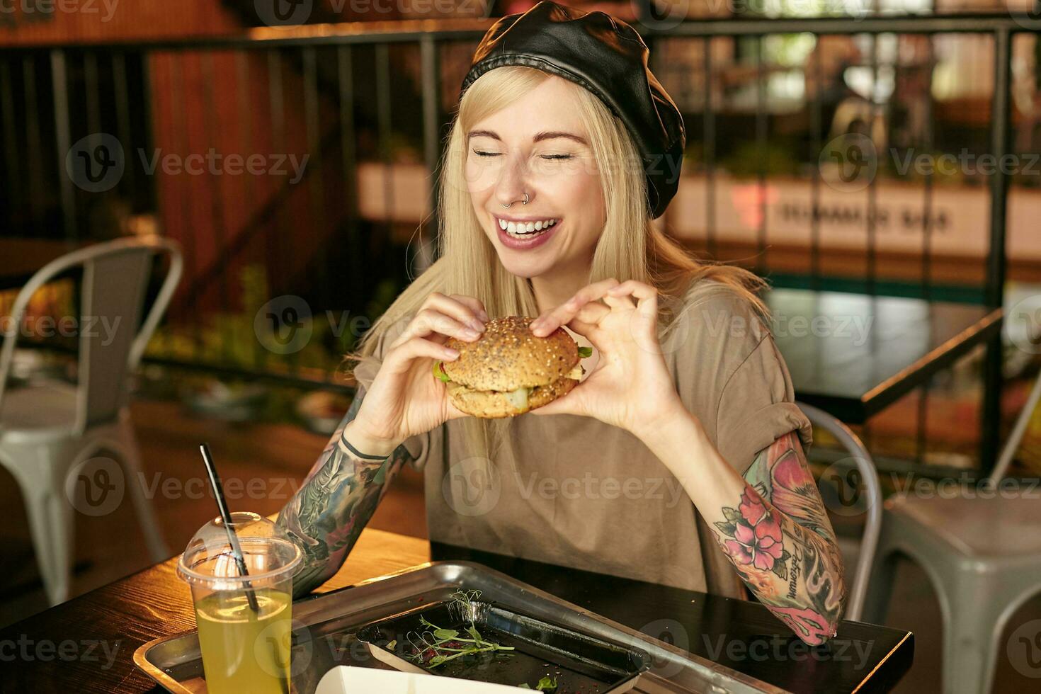 interno foto di gioioso bella donna con bionda lungo in posa al di sopra di bar interno, avendo delizioso pranzo mentre seduta a tavolo, conservazione occhi chiuso con largo e allegro Sorridi