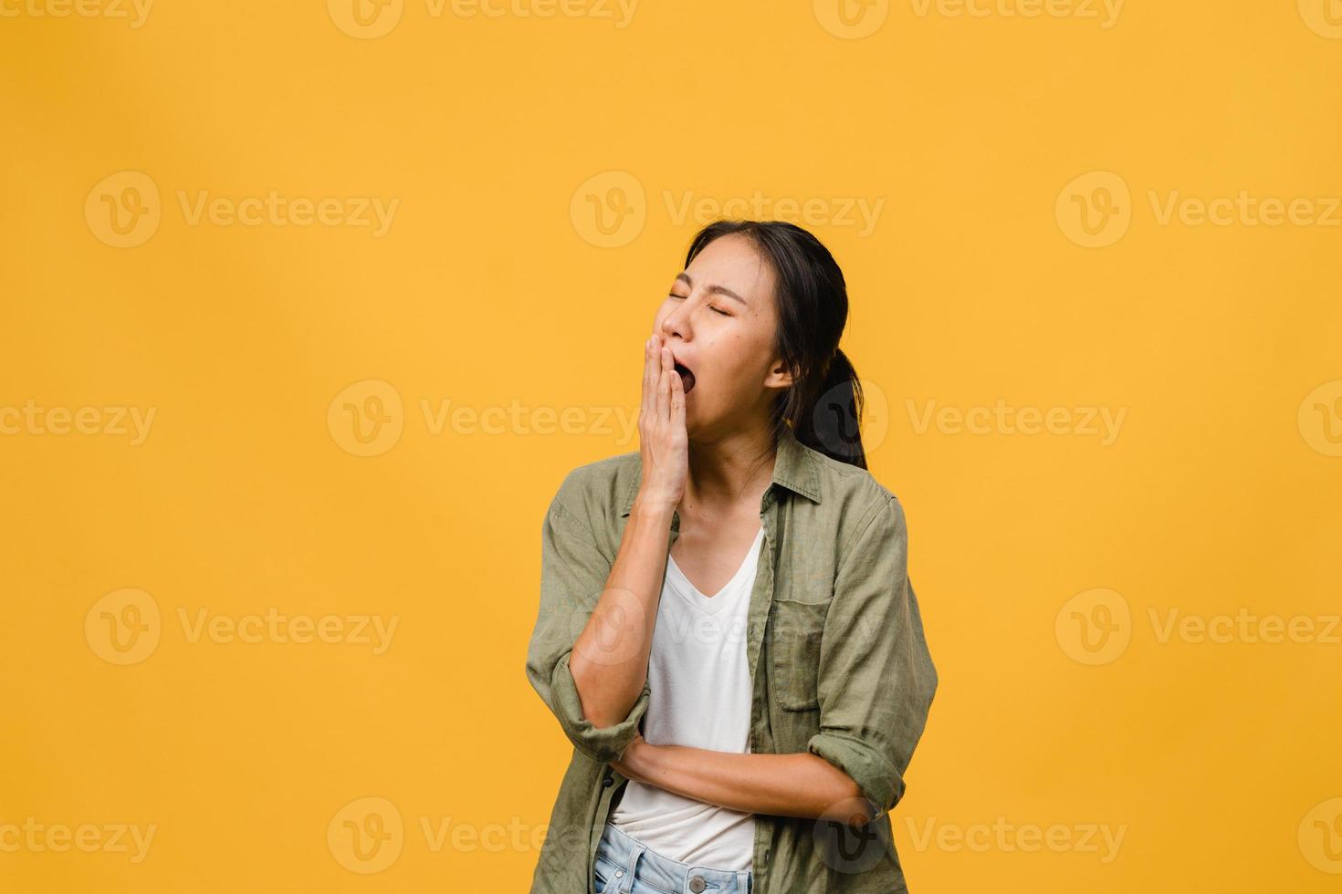 ritratto di giovane donna asiatica con espressione negativa, annoiato sbadigliando stanco che copre la bocca con la mano in abbigliamento casual isolato su sfondo giallo con spazio vuoto per copia. concetto di espressione facciale foto