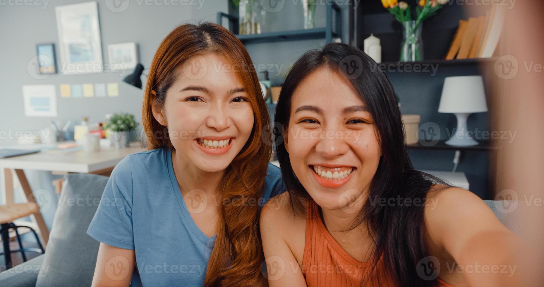 donne asiatiche adolescenti che si sentono selfie sorridenti felici e guardano la telecamera mentre si rilassano nel soggiorno di casa. Videochiamata allegra delle signore del compagno di stanza con l'amico e la famiglia, concetto di stile di vita della donna a casa. foto