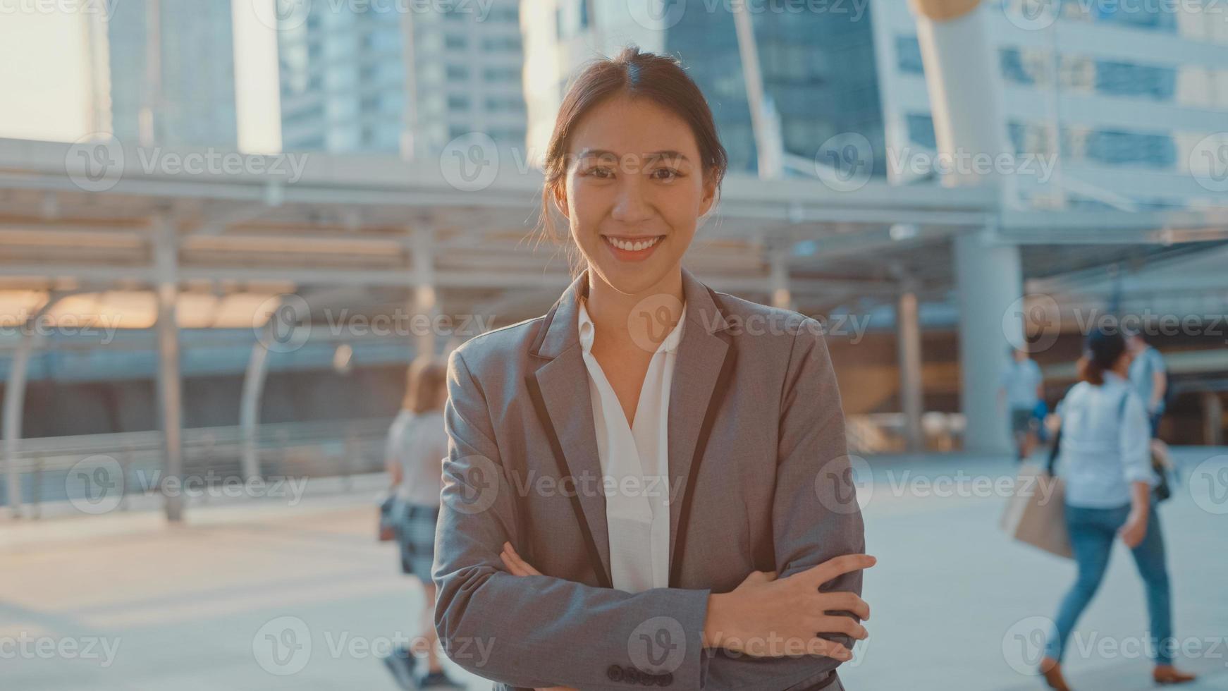 successo giovane donna d'affari asia in abiti da ufficio moda sorridente e guardando la fotocamera mentre felice in piedi da solo all'aperto nella città moderna urbana al mattino. concetto di affari in movimento. foto