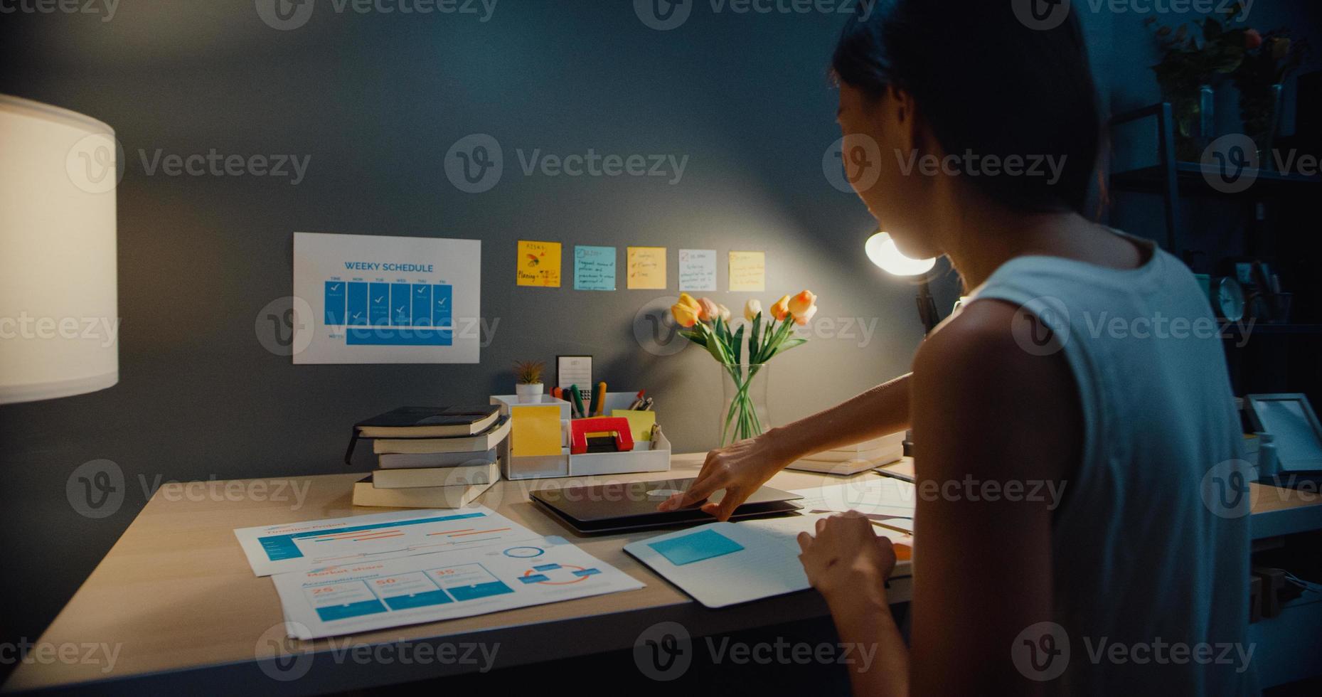giovane asia business lady freelance aperto computer portatile si prepara per iniziare a lavorare sulla scrivania in legno nel soggiorno di casa notte. lavoro da casa, da remoto, quarantena a distanza sociale per coronavirus. foto