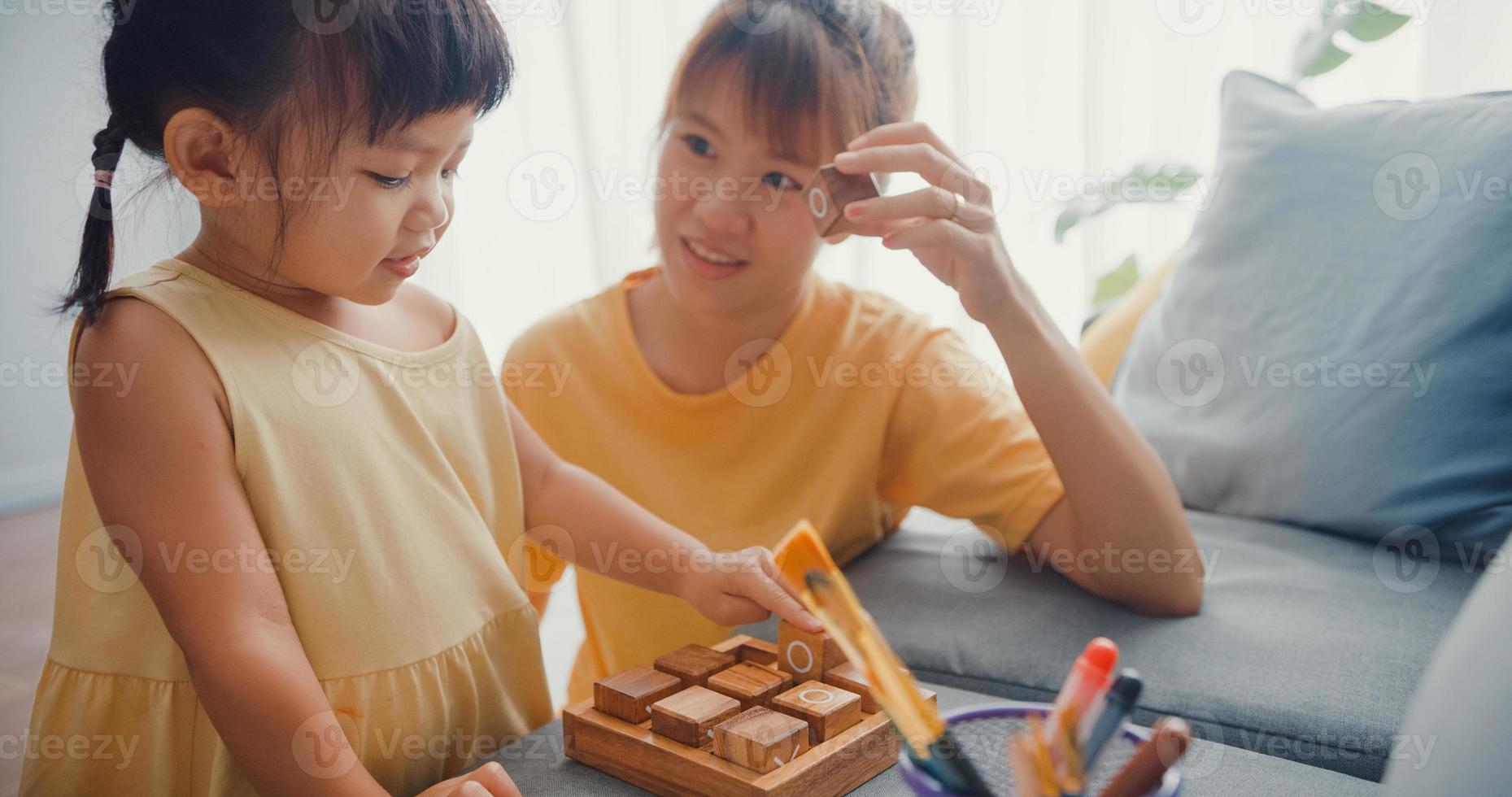 felice allegra famiglia asia mamma insegna alla ragazza a giocare a un gioco da tavolo hobby con una scatola di legno che si diverte a rilassarsi sul divano nel soggiorno di casa. passare del tempo insieme, distanza sociale, quarantena per il coronavirus. foto