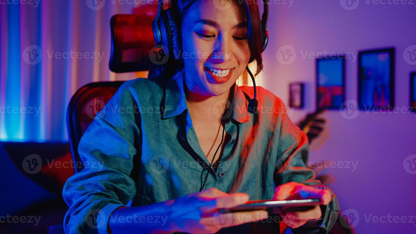 felice asia ragazza giocatore indossa la competizione per le cuffie gioca al videogioco online con smartphone luci al neon colorate nel soggiorno di casa. gioco in streaming di esport online, concetto di attività di quarantena domestica. foto