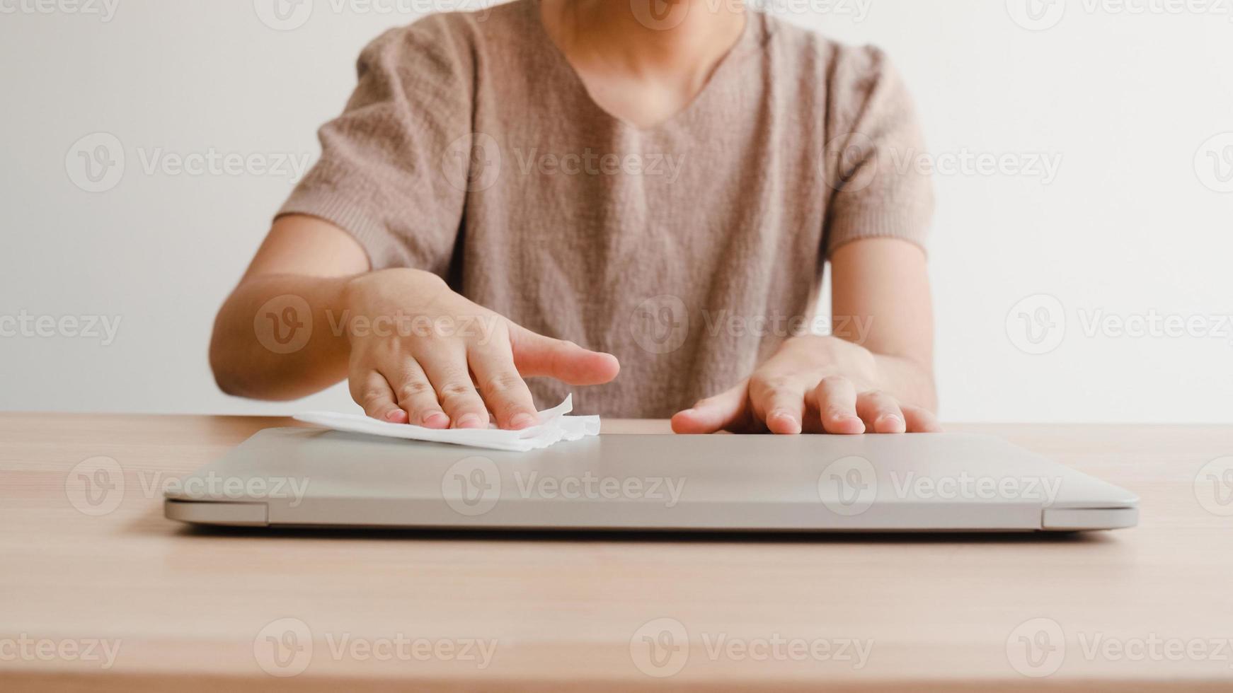 donna asiatica che usa spray alcolico su un laptop pulito in tessuto prima dell'apertura per proteggere il coronavirus. computer pulito femminile per l'igiene quando il distanziamento sociale resta a casa e il tempo di autoquarantena. foto