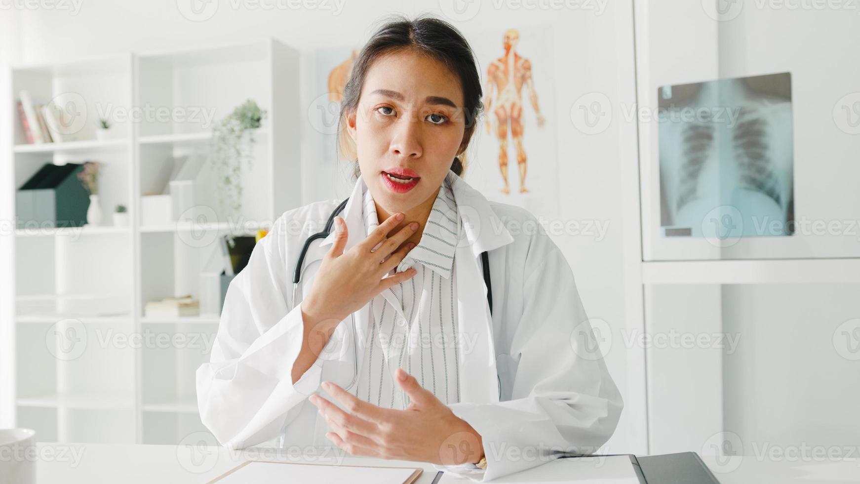 giovane dottoressa asiatica in uniforme medica bianca con stetoscopio utilizzando il computer portatile parla in videoconferenza con il paziente, guardando la telecamera in ospedale sanitario. concetto di consulenza e terapia. foto