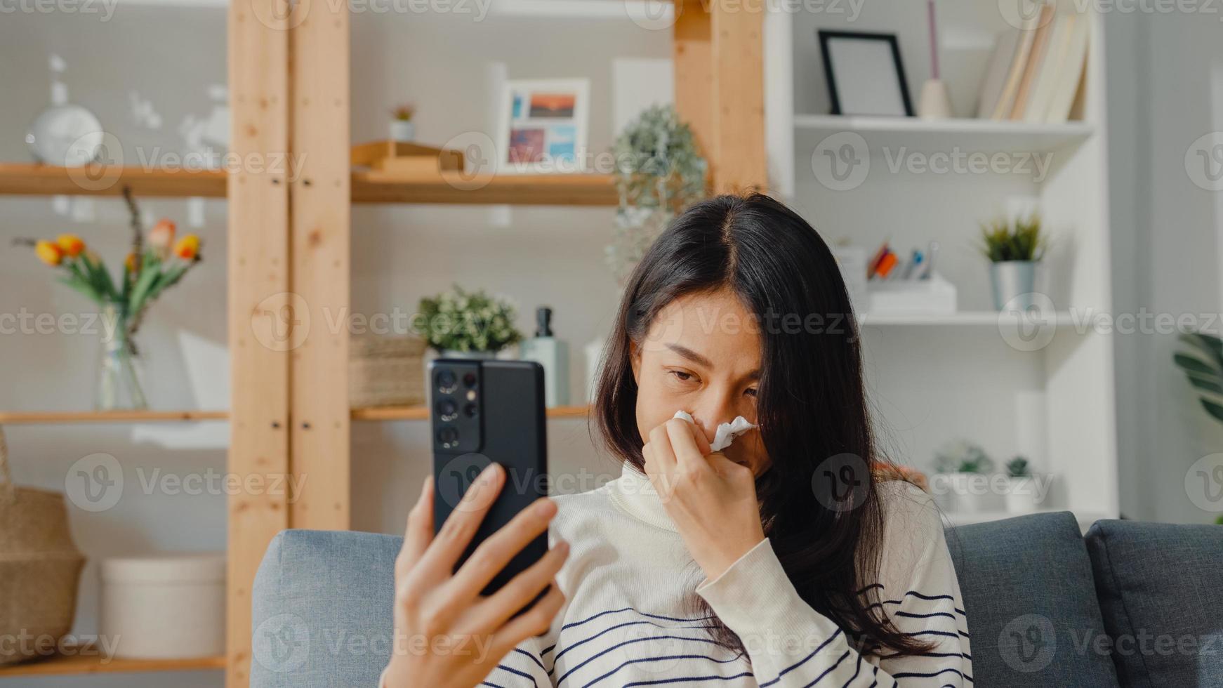 malata giovane donna asiatica tenere la medicina sedersi sul divano videochiamata con il telefono consultare il medico a casa. la ragazza prende la medicina dopo l'ordine del medico, la quarantena a casa, il concetto di coronavirus di distanza sociale. foto