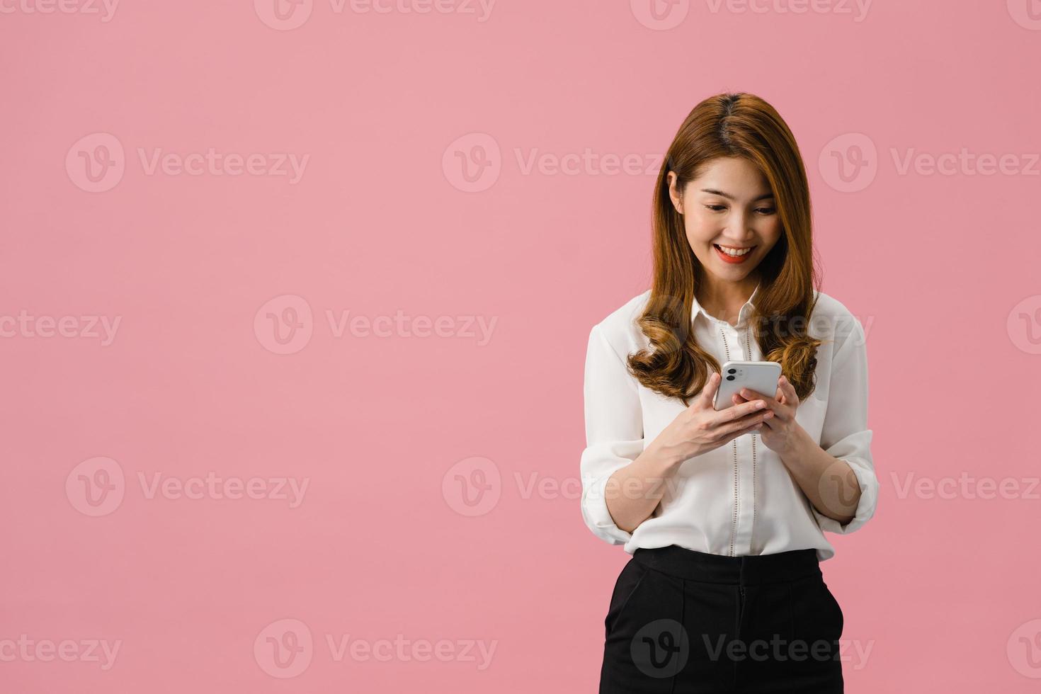 giovane donna asiatica che usa il telefono con espressione positiva, sorride ampiamente, vestita con abiti casual, sentendosi felice e in piedi isolato su sfondo rosa. felice adorabile donna felice esulta successo. foto