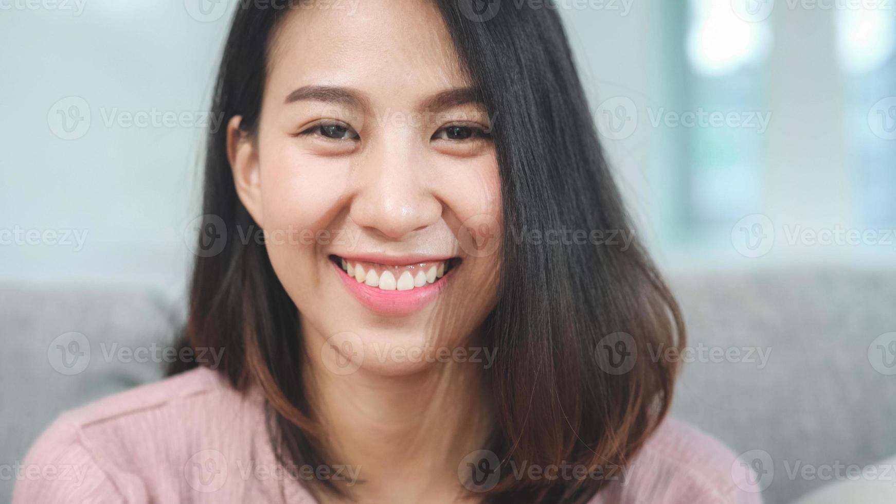 adolescente donna asiatica sentirsi felice sorridente e guardando la telecamera mentre si rilassa nel soggiorno di casa. stile di vita bella giovane donna asiatica che utilizza il concetto di tempo di relax a casa. foto